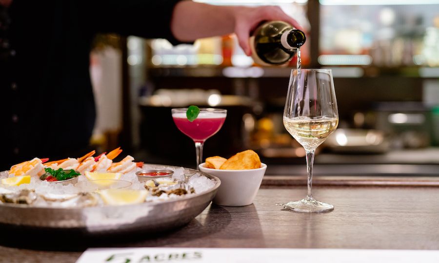 Hand pouring a glass of white wine at 5 Acres