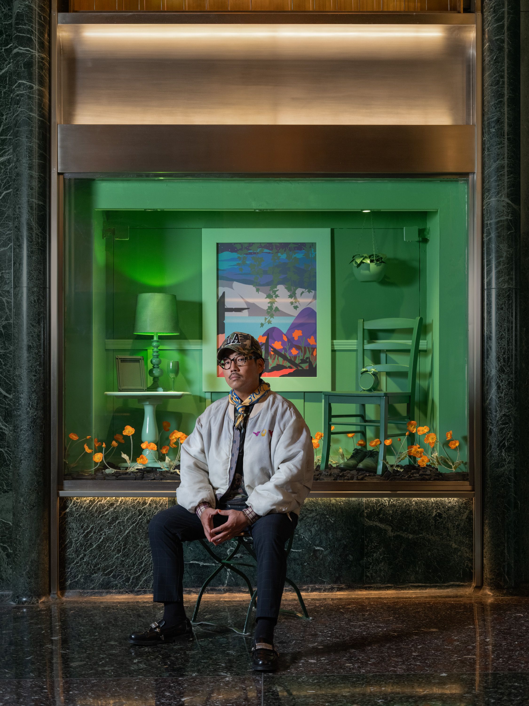 Artist Greg Ito sitting in front of a vitrine with his artwork