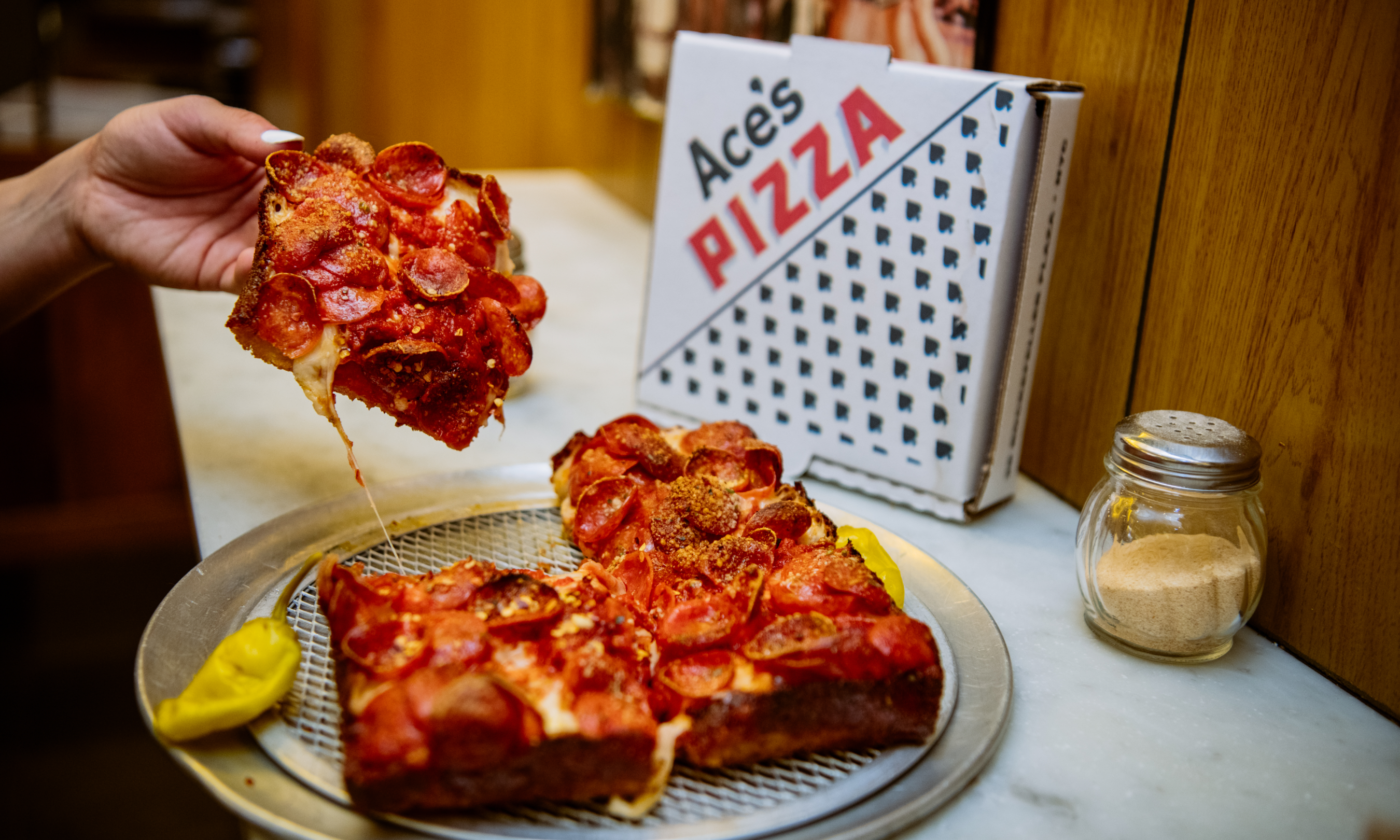 Hand grabbing a slice of pizza from Ace's Pizza