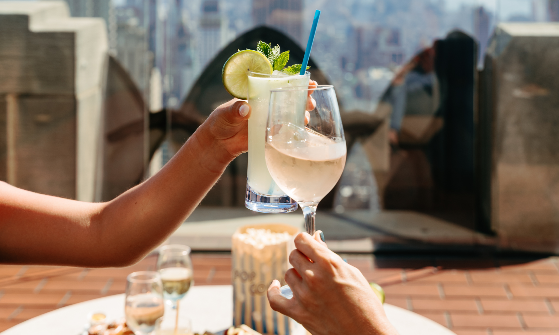 Two hands clinking cocktail glasses at The Weather Room at Top of the Rock