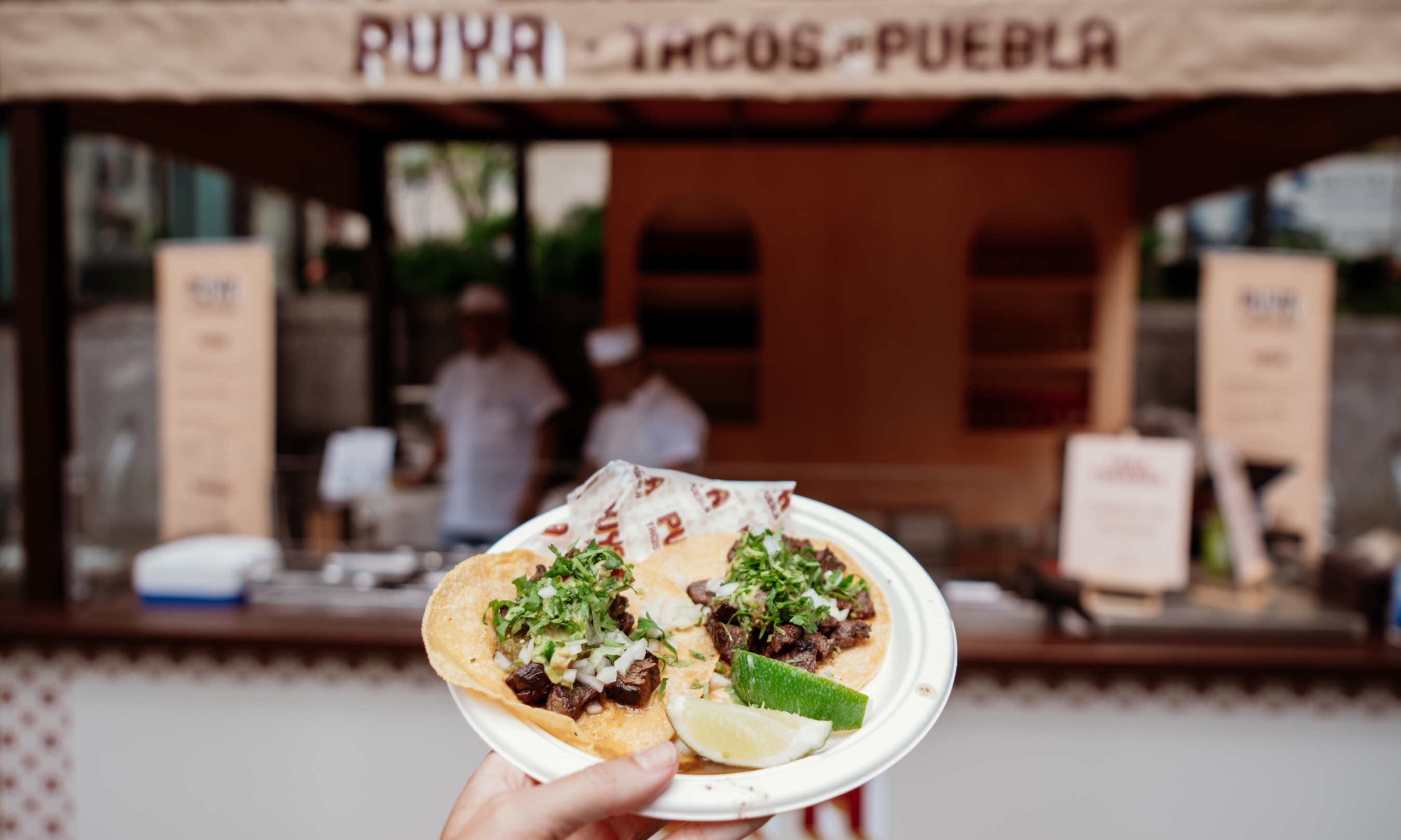 A hand holding a plate of tacos from Puya Tacos at Rockefeller Center