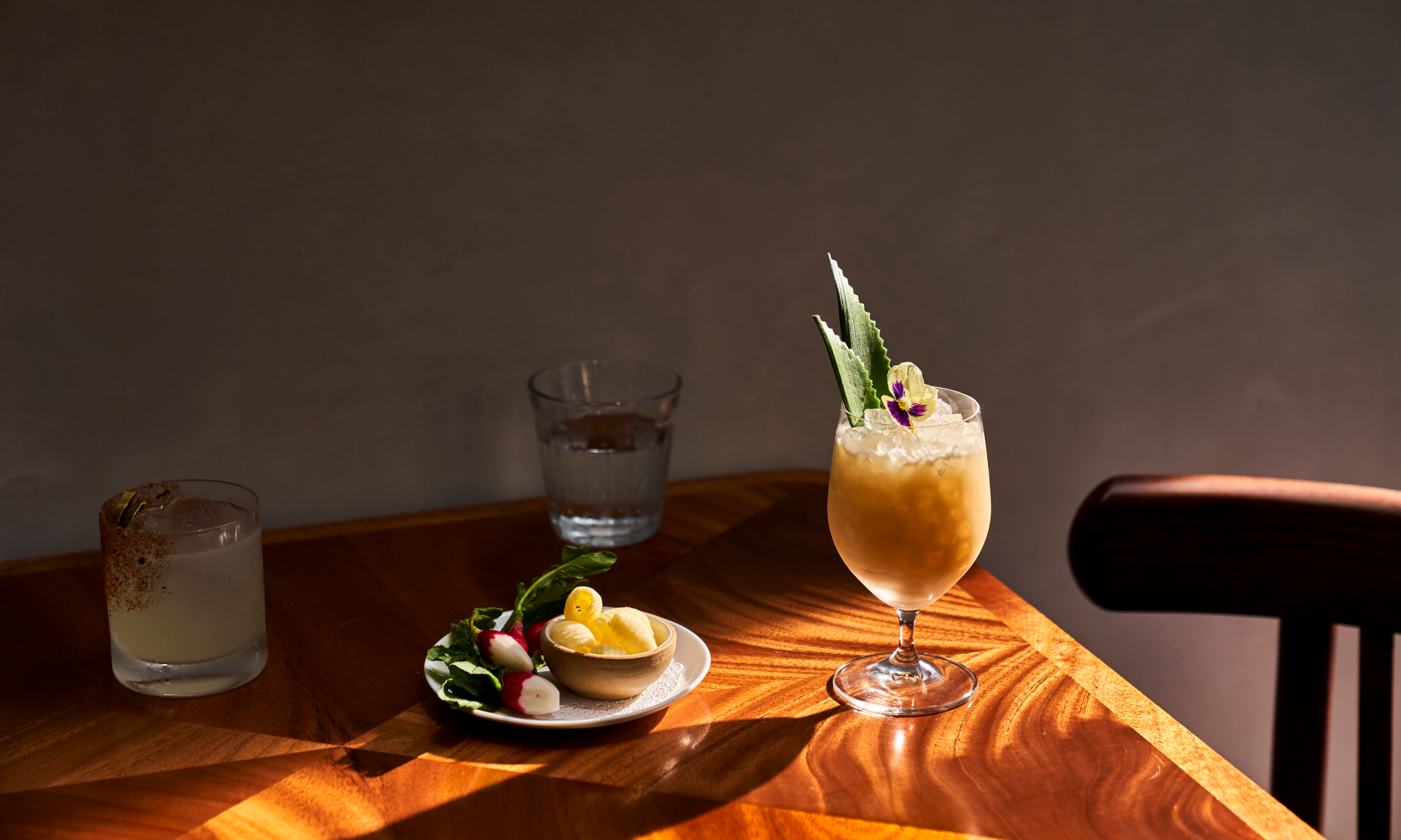 A plate of appetizers, a glass of water, and two cocktails on a table at Le Rock