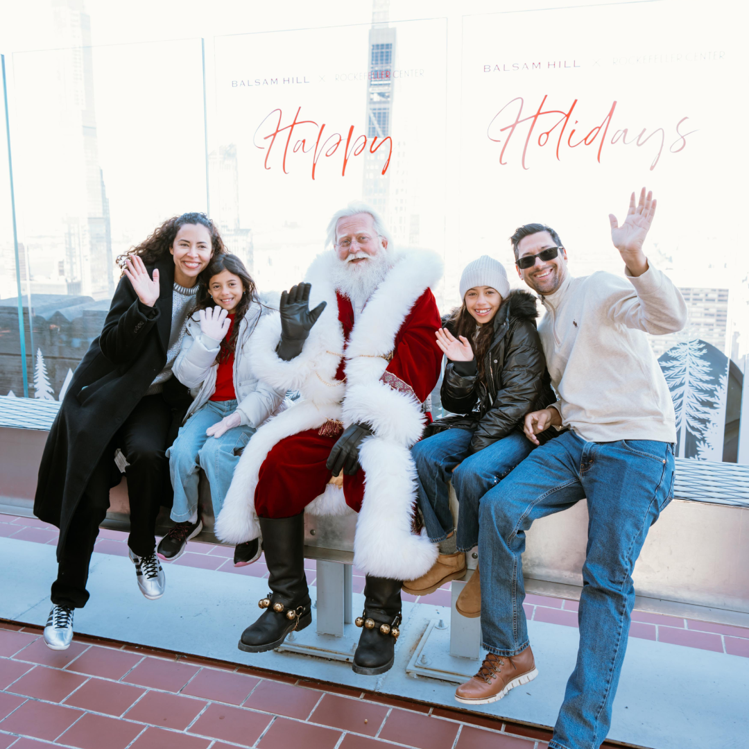 A family of four posing for a photo with Santa Claus on The Beam at Top of the Rock