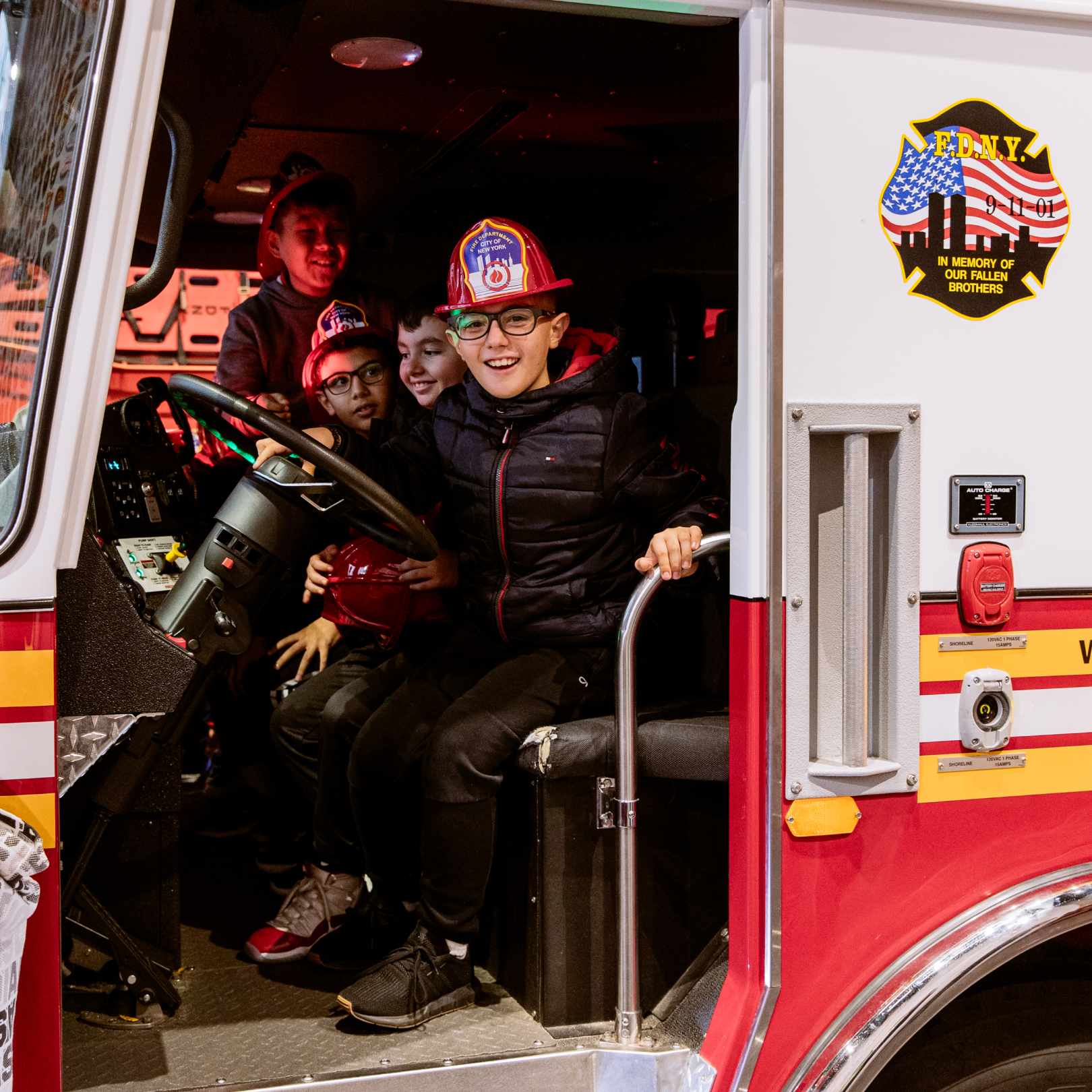 Four kids sitting in a fire truck at Rockefeller Center's FDNY Fire Zone