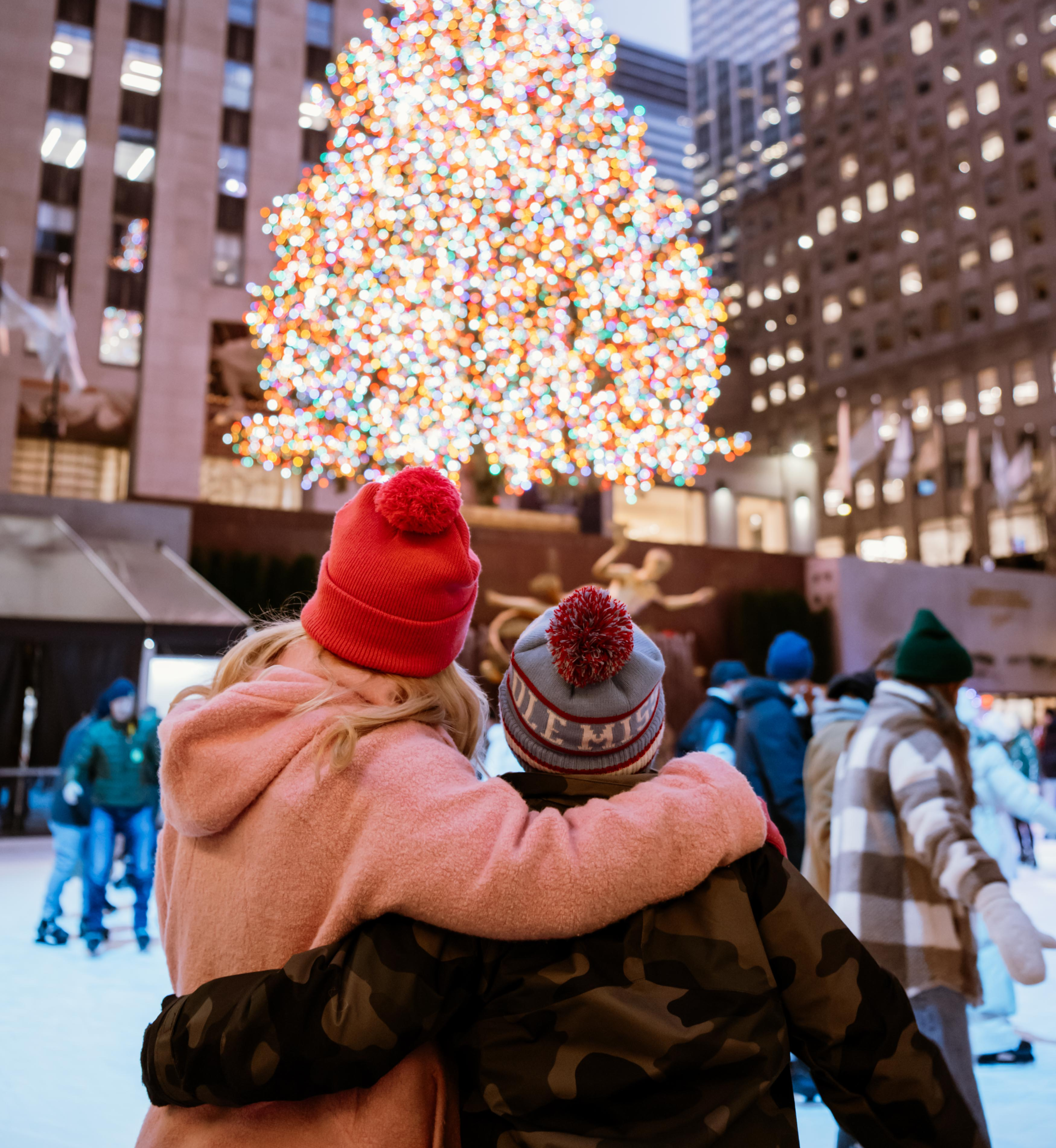 Two people looking at the Rockefeller Center Christmas Tree above The Rink
