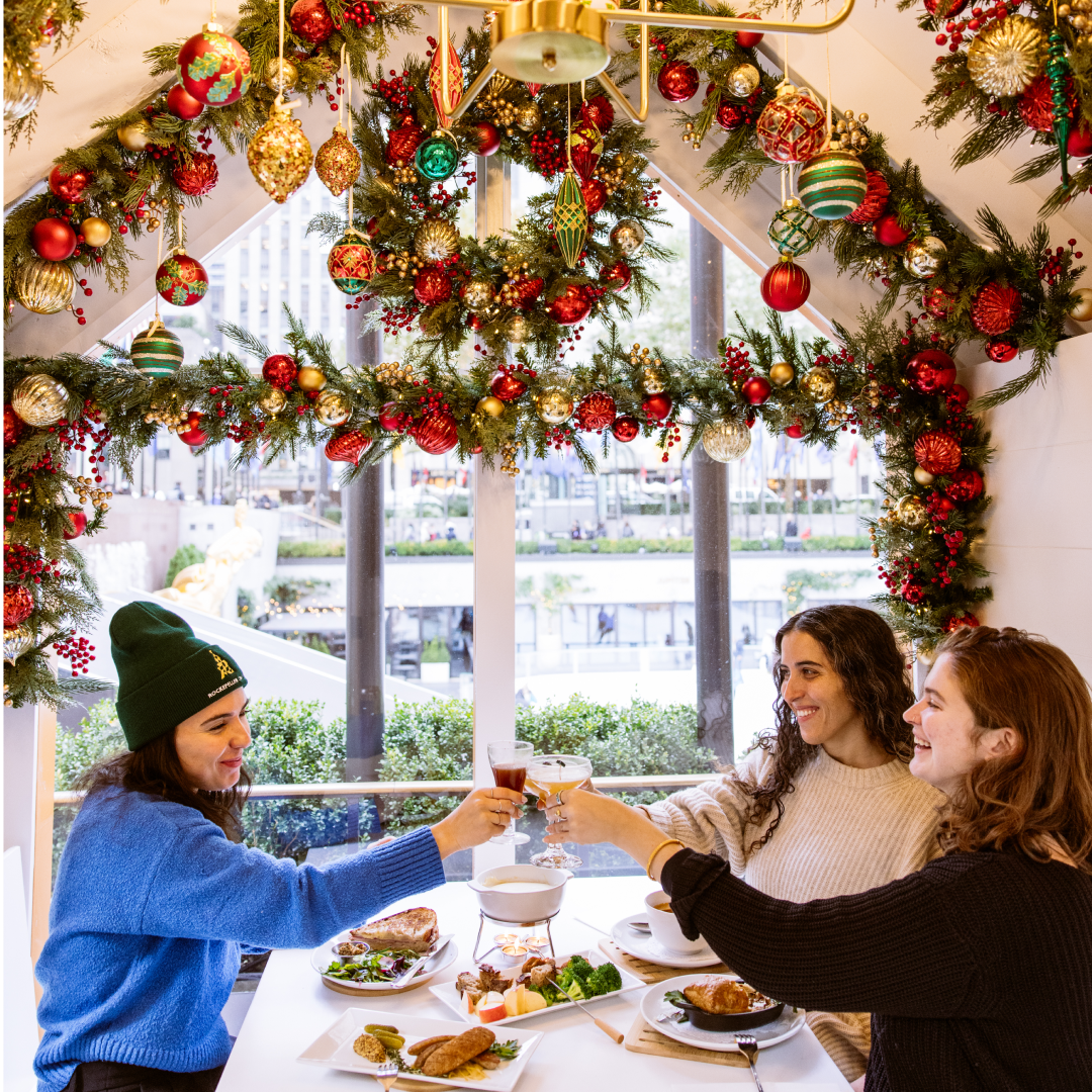 Three women sharing drinks and light bites inside Rockefeller Center's Après Skate Chalets