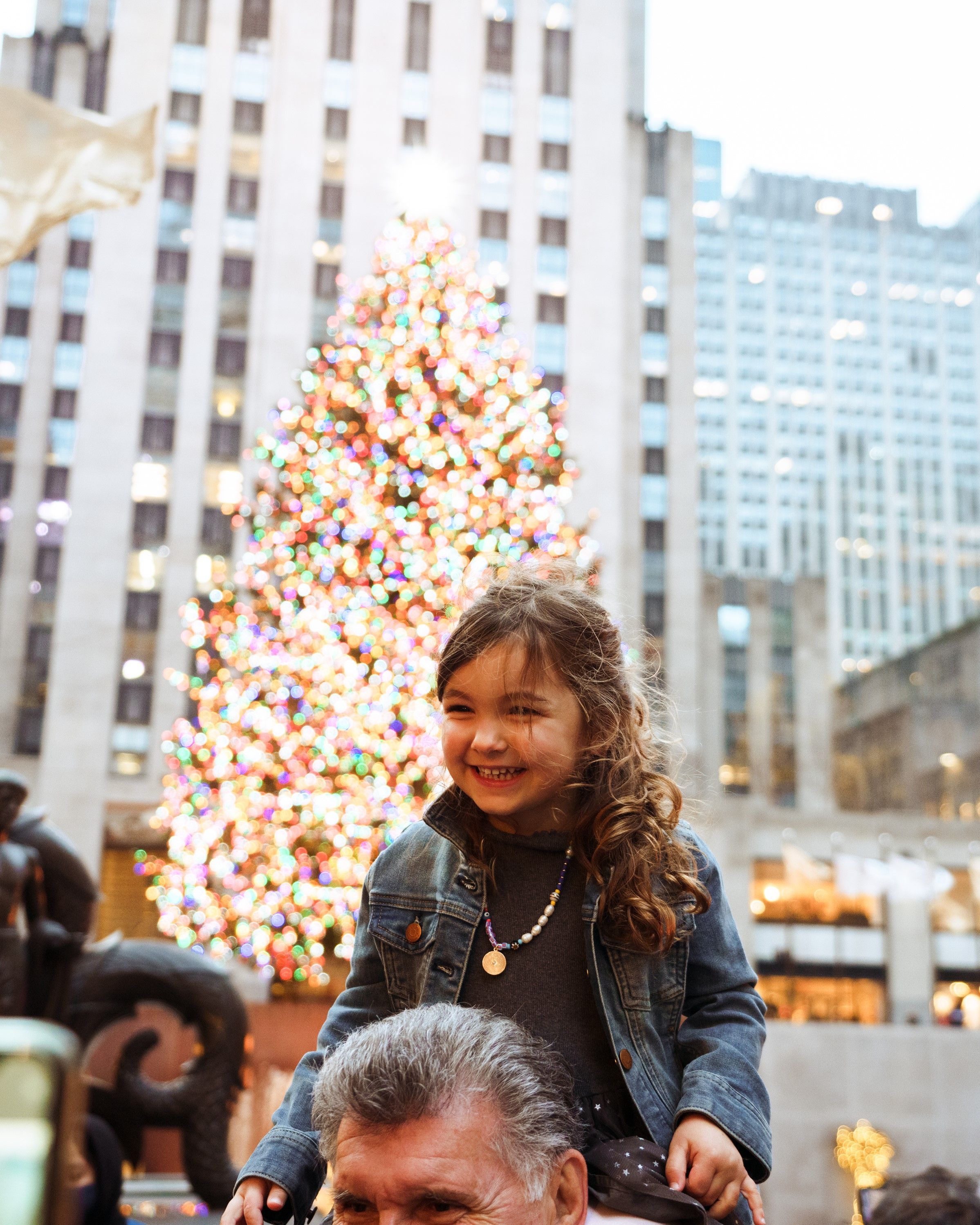 a girl smiling in front of the rockefeller center christmas tree
