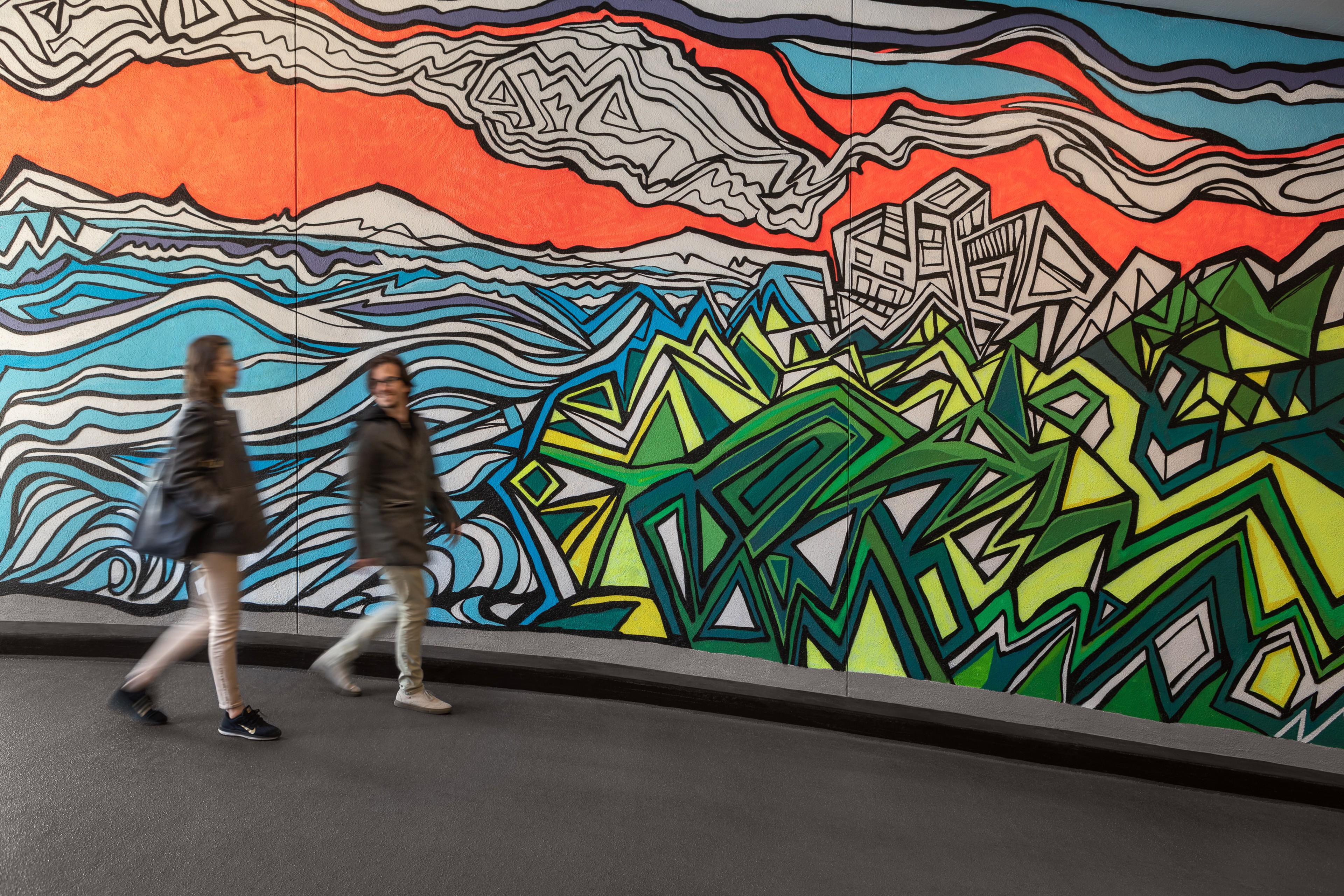 Two people walking in front of a colorful mural