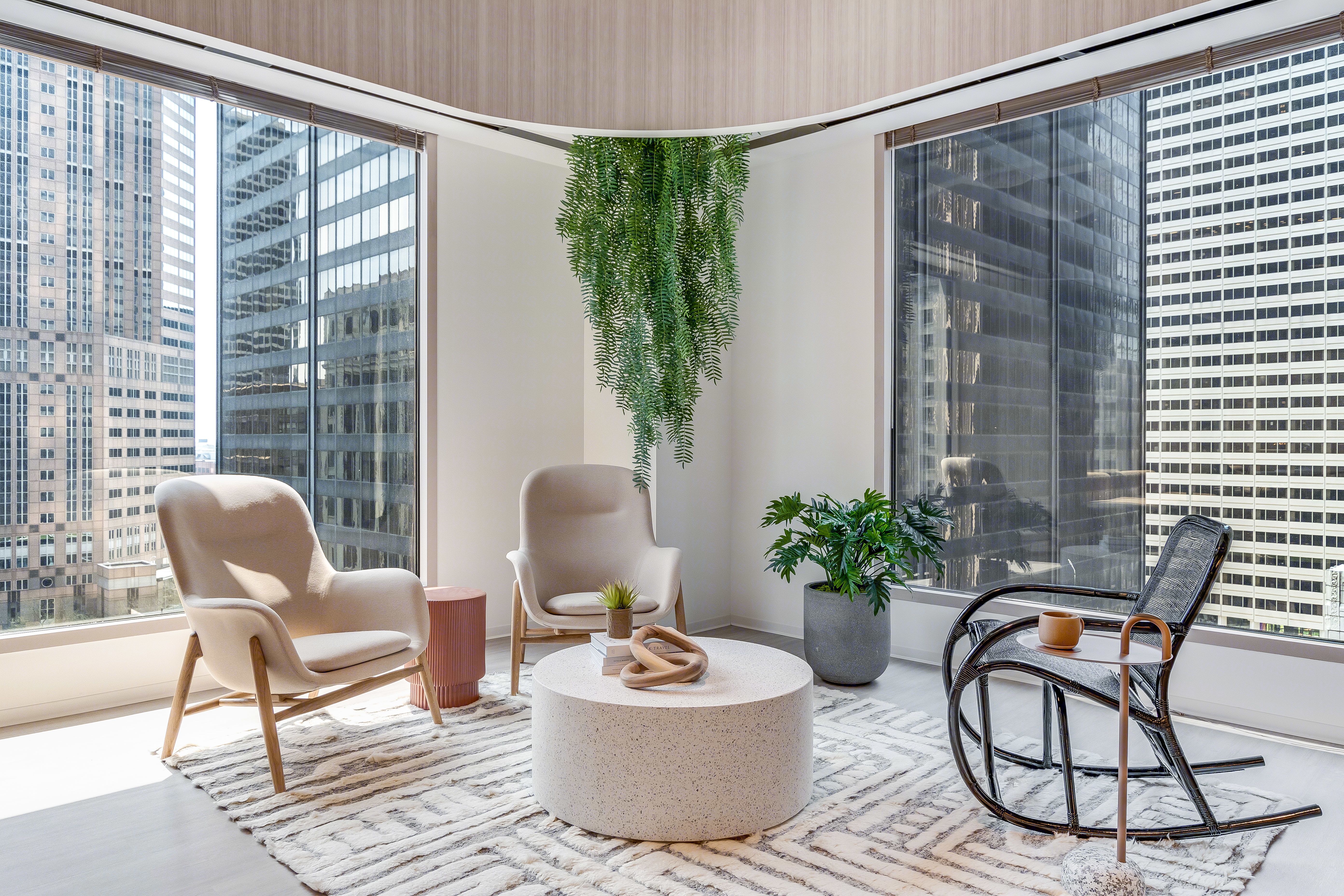Modern office lounge with large windows, comfortable chairs, round table, and green plants