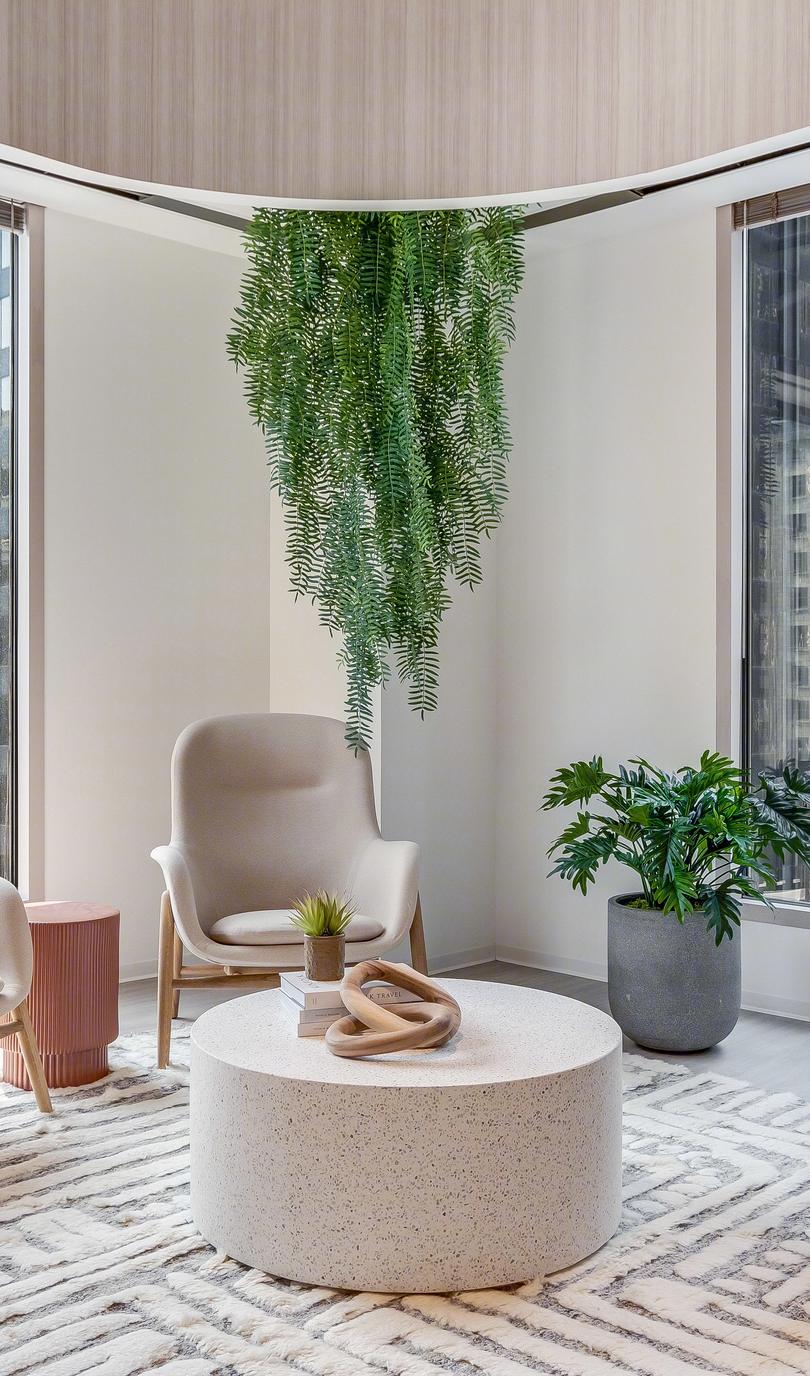 Modern office lounge with large windows, comfortable chairs, round table, and green plants