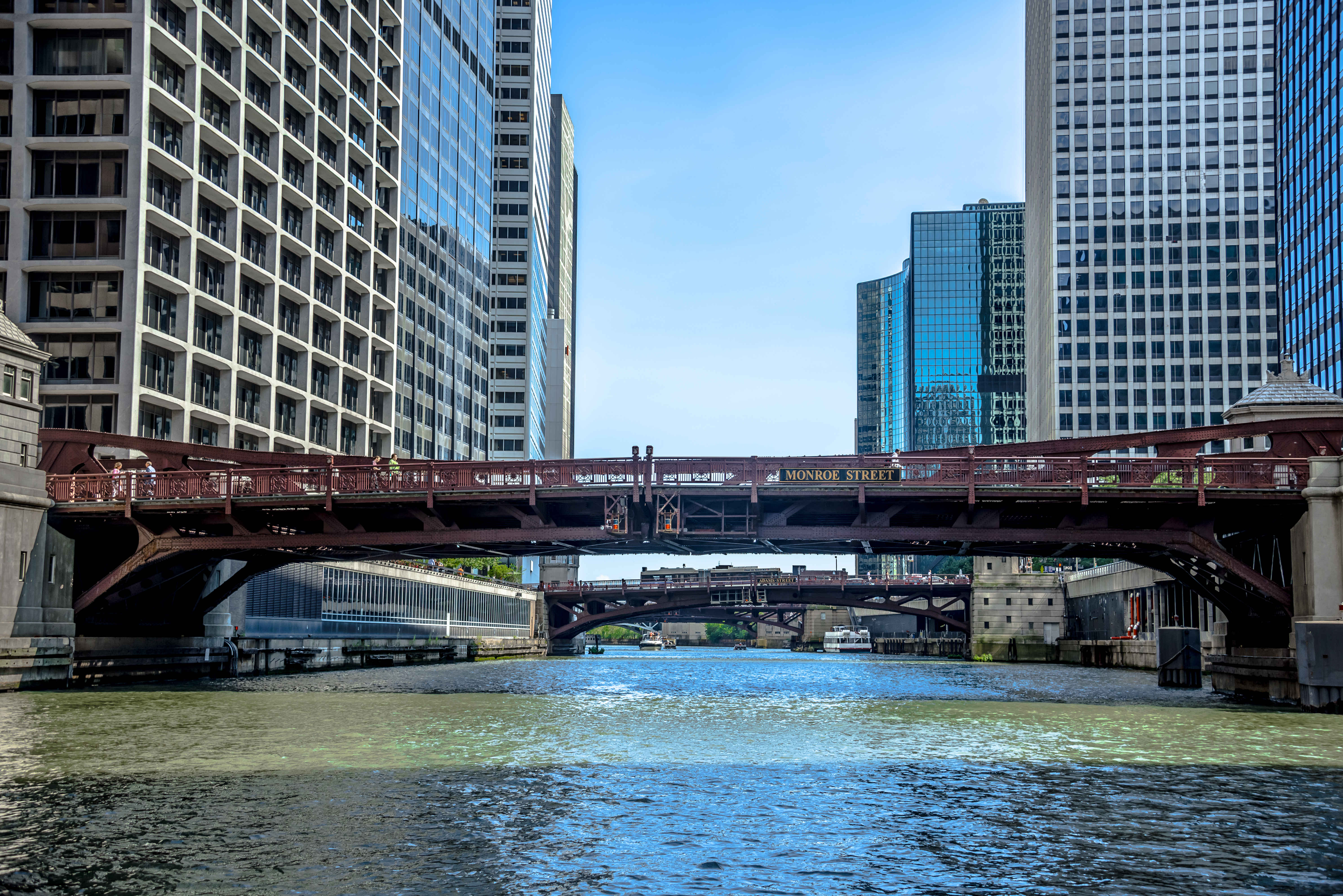 View of the Chicago River near 525 West Monroe, with downtown high-rise buildings and multiple steel bridges crossing the water under a clear blue sky.