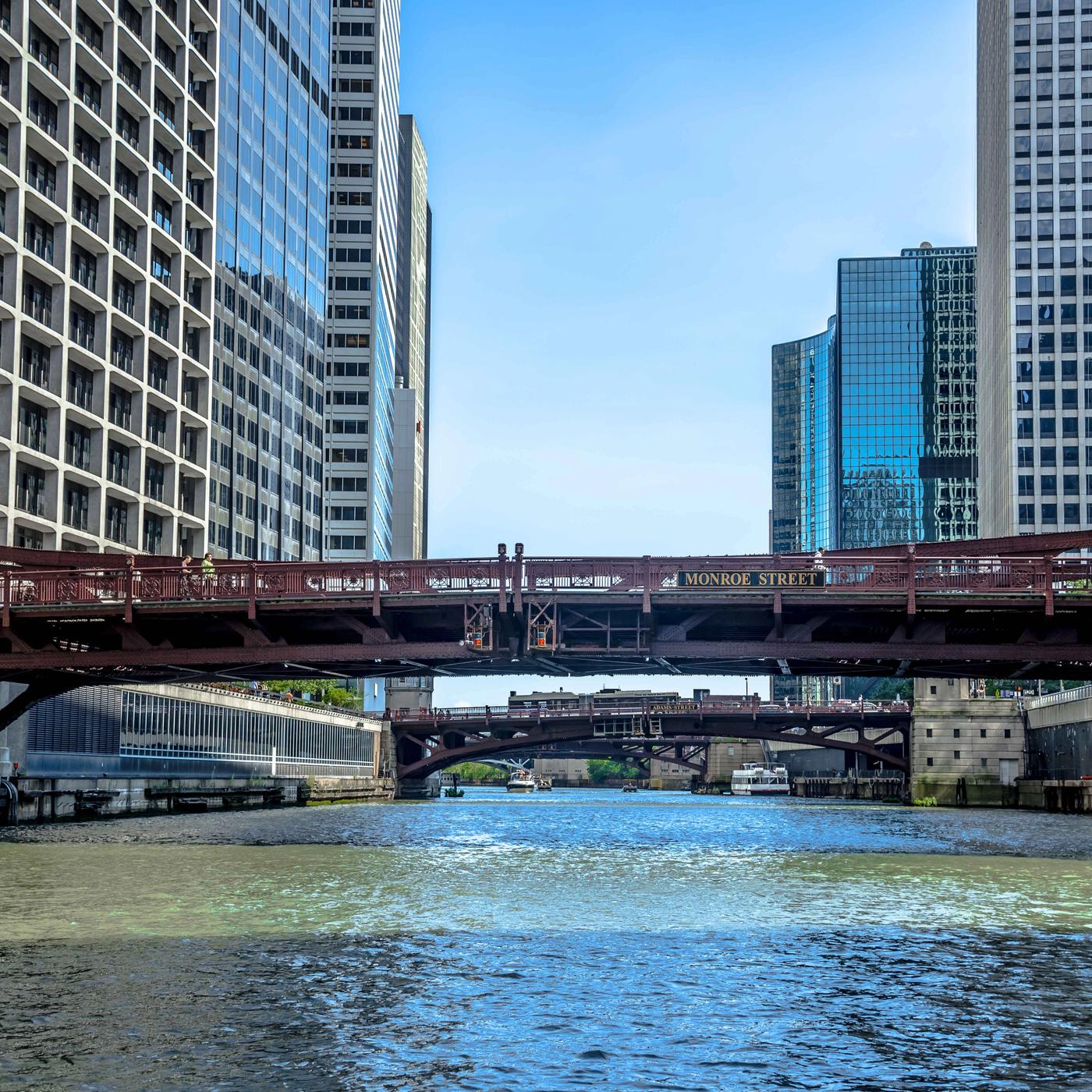 View of the Chicago River near 525 West Monroe, with downtown high-rise buildings and multiple steel bridges crossing the water under a clear blue sky.