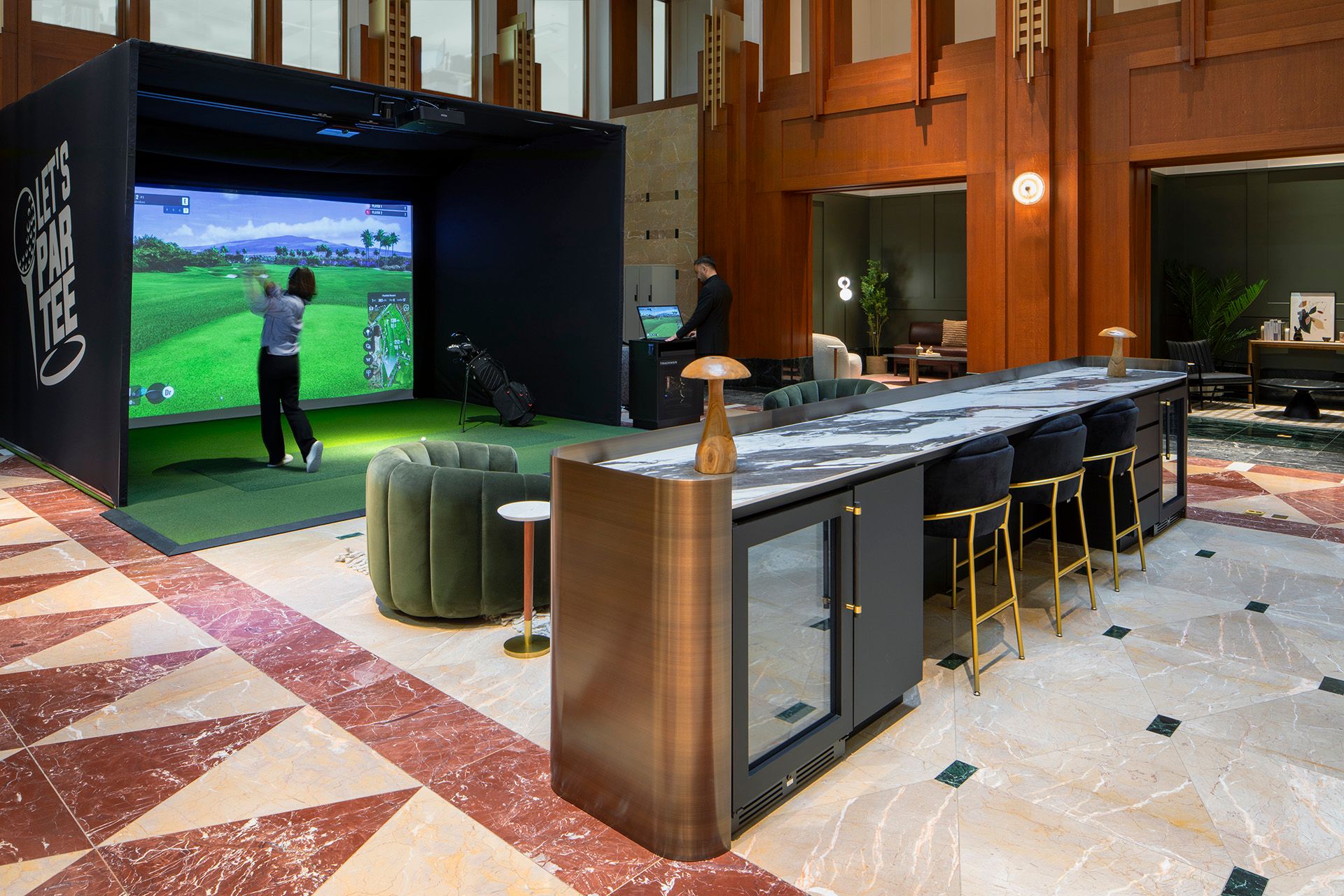 Indoor golf simulator setup next to a modern lounge area with a marble and wood countertop and seating.