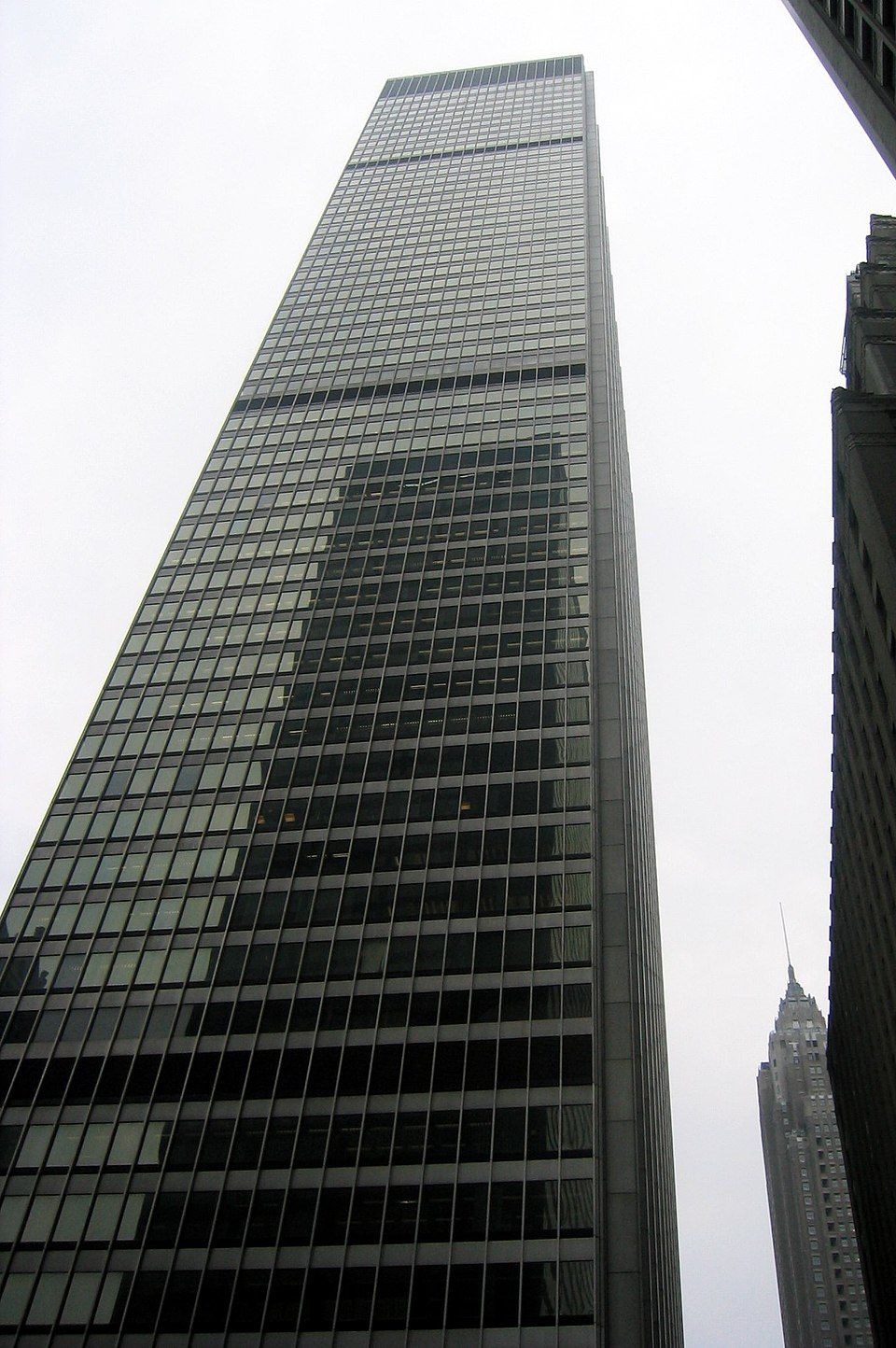 A gray skyscraper with numerous windows dominates the image, reflecting the surrounding cityscape and creating a sense of depth.