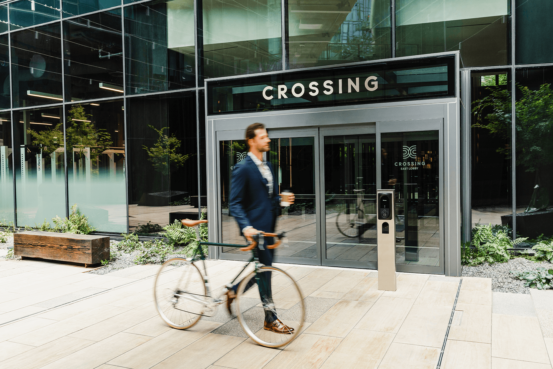Someone walking their bike in front of the entrance to Crossing DC apartments in Navy Yard, featuring large glass doors.