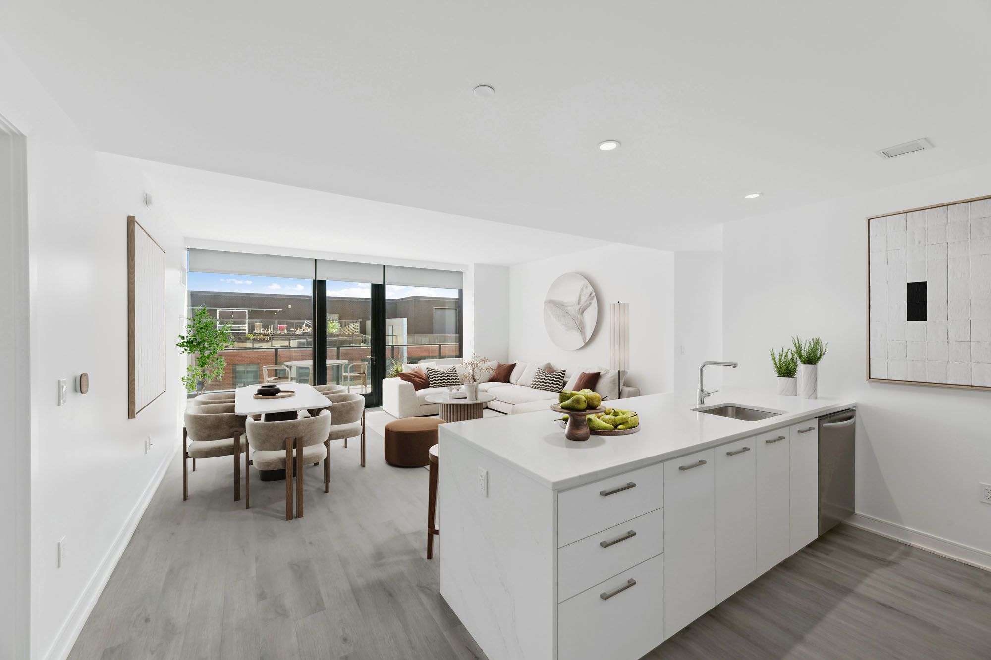 Model kitchen and living room at Crossing DC apartments in Navy Yard, featuring wood grain floor paneling and large windows.