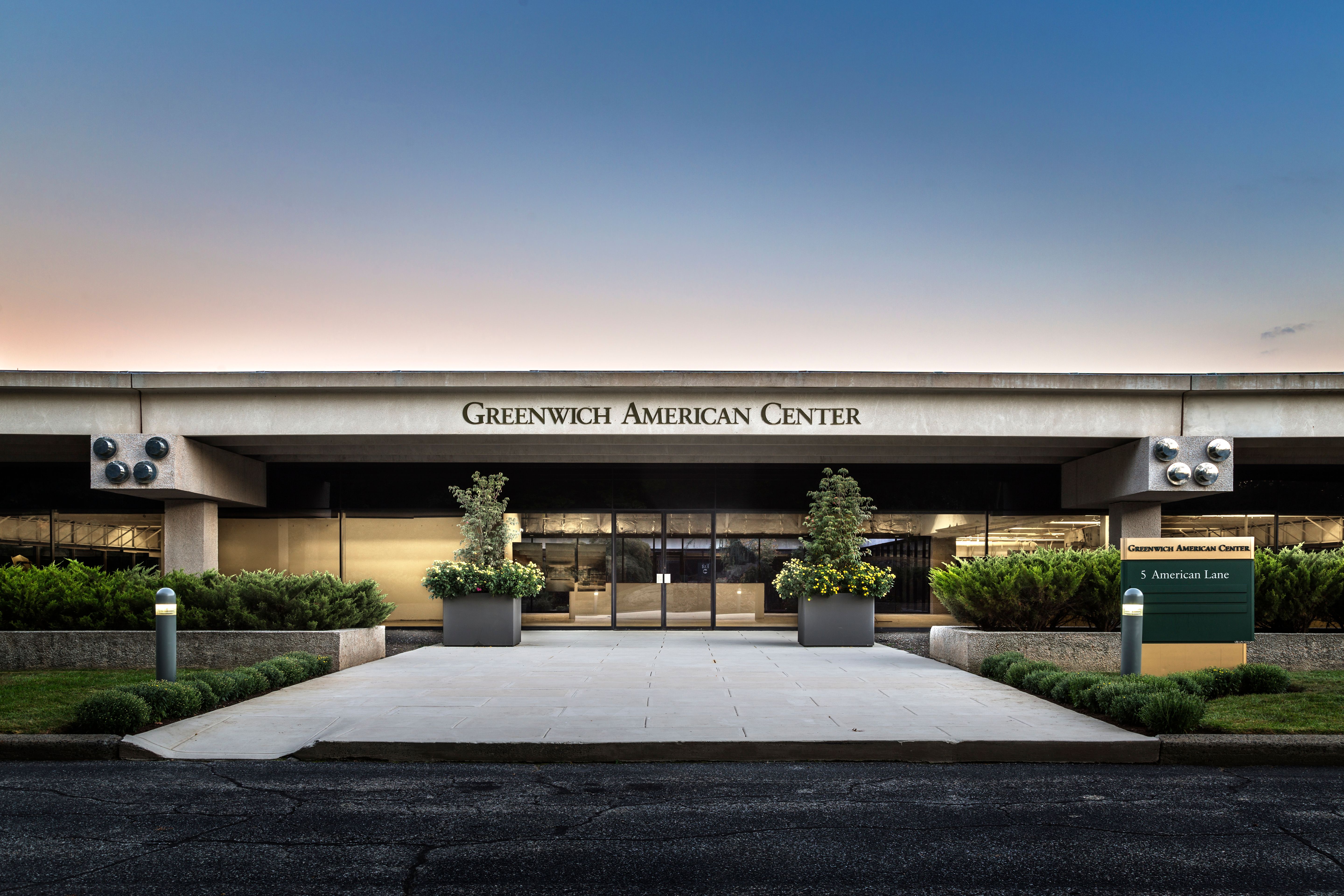The image shows the entrance of the Green American Center, featuring a modern facade, large glass doors, and a well-maintained sidewalk.