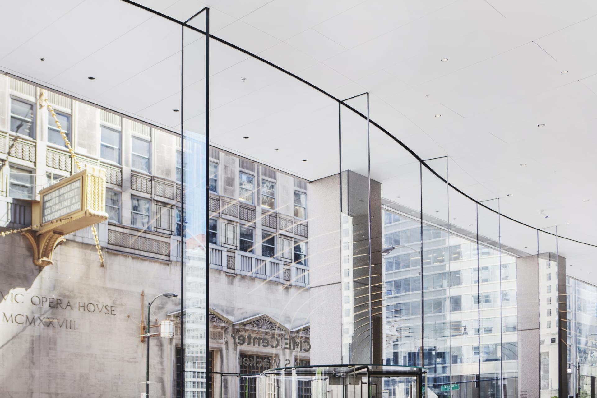 A modern glass and steel building with a glass facade, reflecting a cityscape, is located in a bustling urban area.