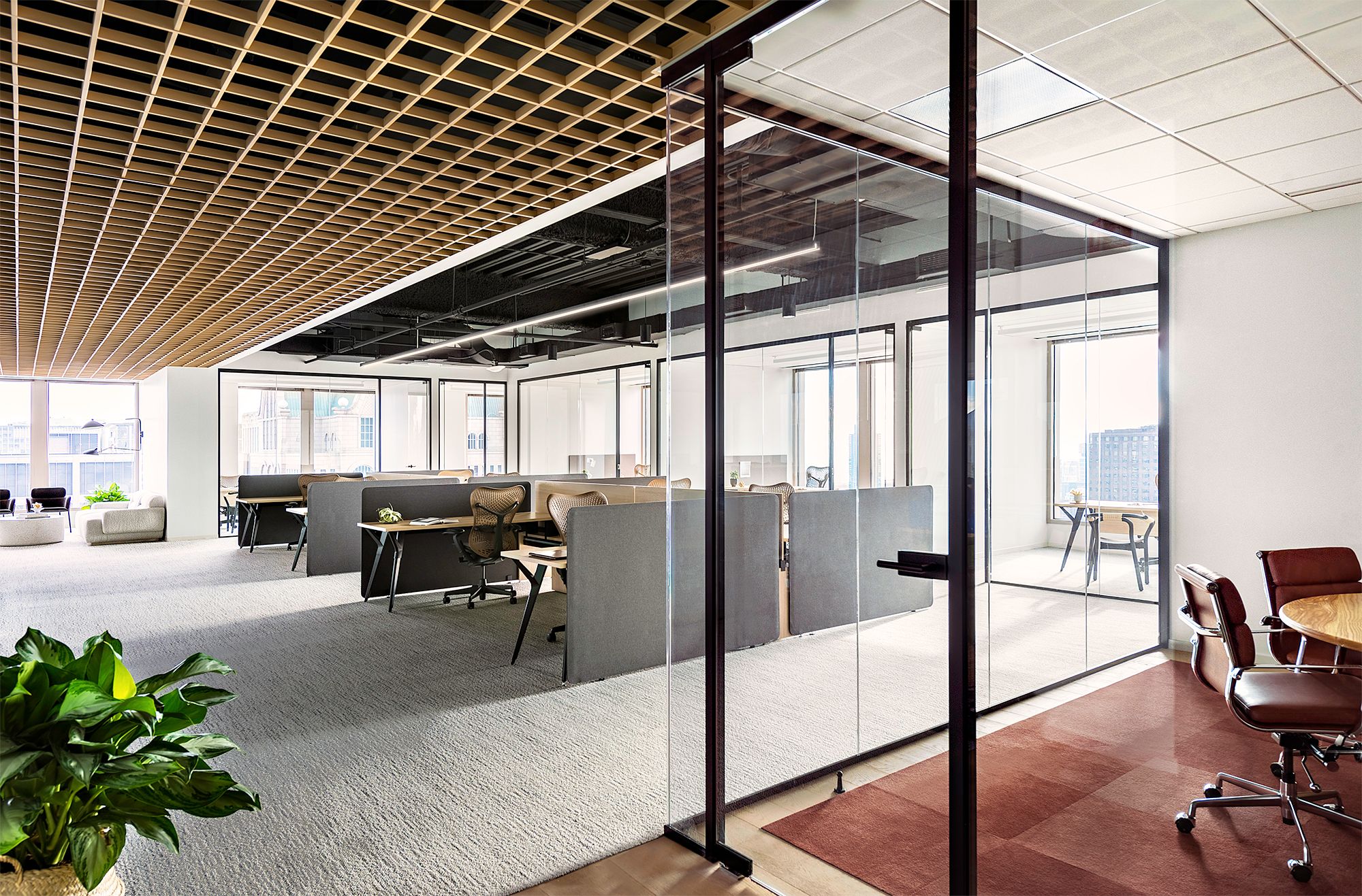 Bright modern office space with open workstations, glass meeting room, and comfortable seating areas