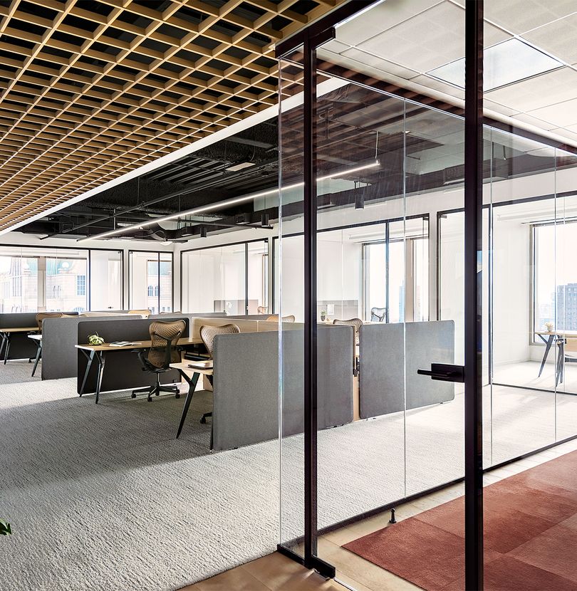 Bright modern office space with open workstations, glass meeting room, and comfortable seating areas