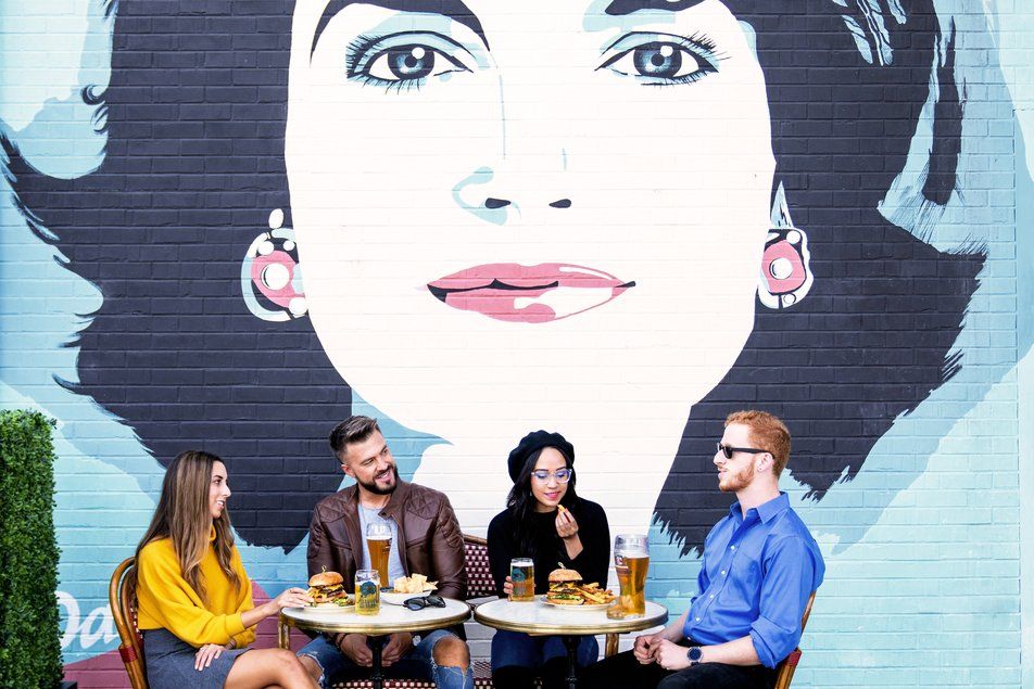 Residents eating at an outdoor dining area near Crossing DC apartments in Navy Yard, featuring a mural in the background.