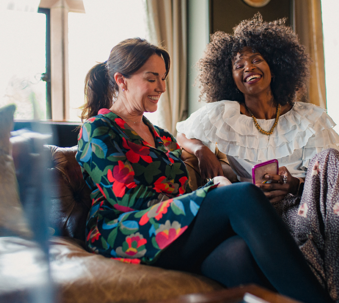 Lifestyle image for 525 West Monroe marketing, showing two people sitting on a sofa indoors, smiling and talking while one holds a smartphone.