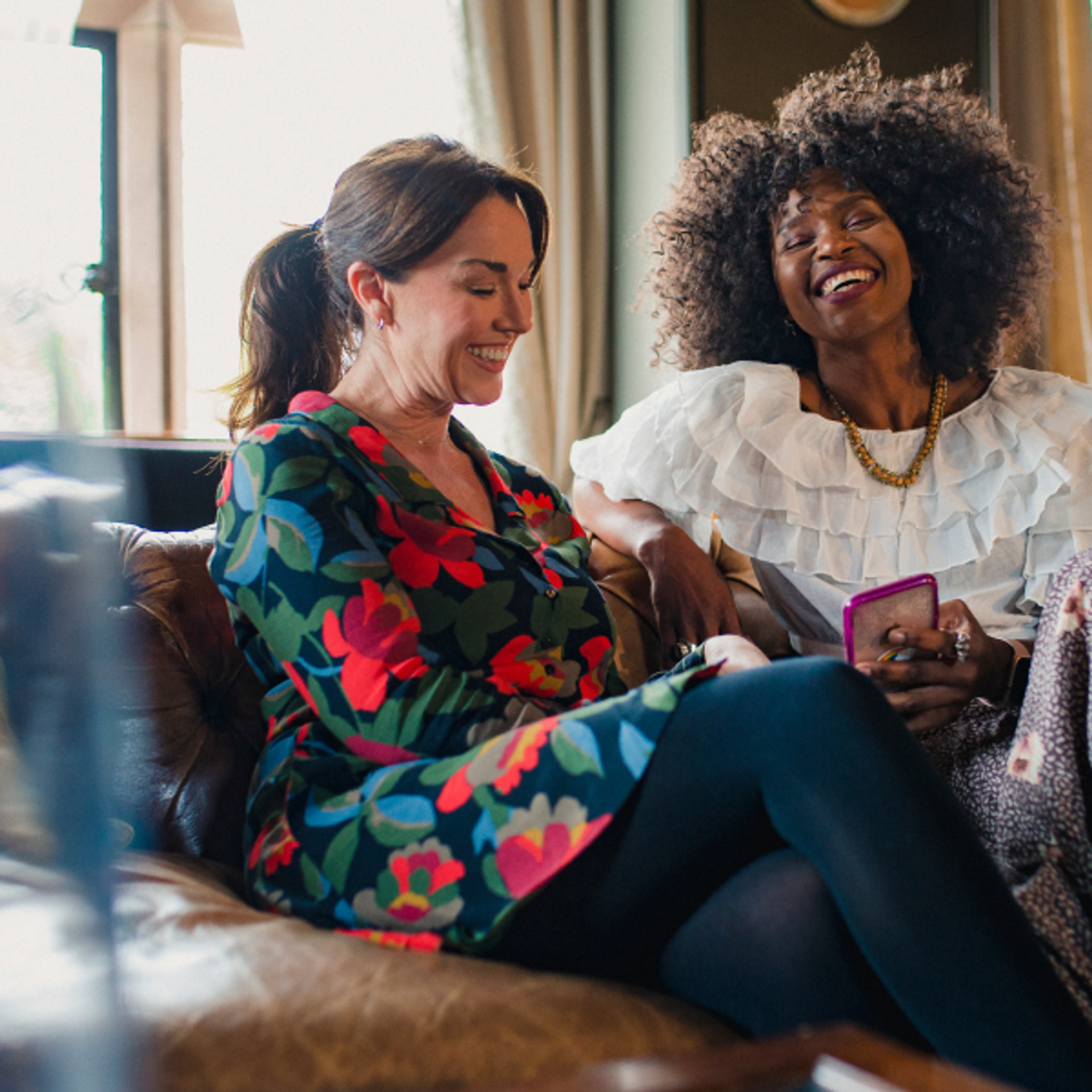 Lifestyle image for 525 West Monroe marketing, showing two people sitting on a sofa indoors, smiling and talking while one holds a smartphone.
