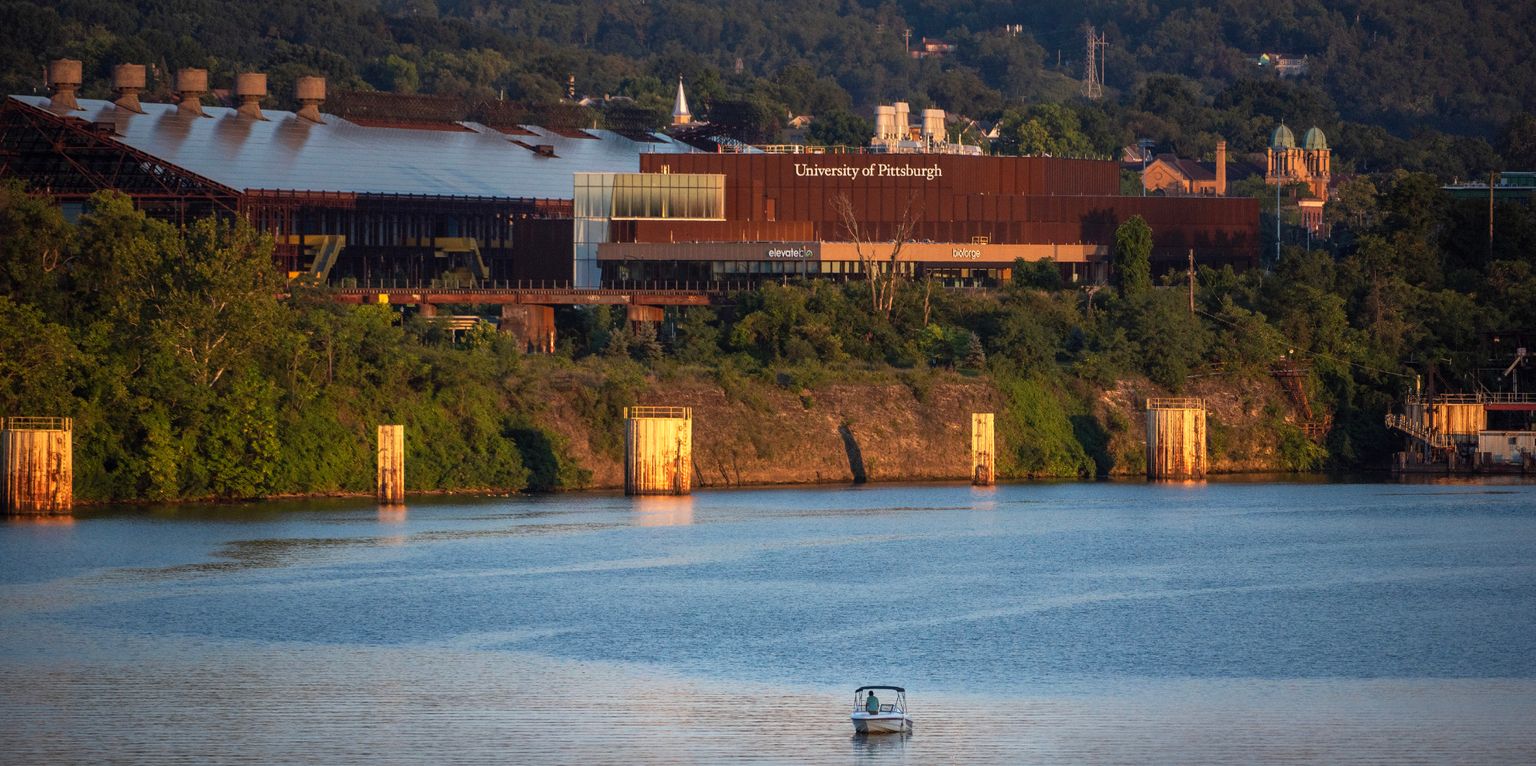 view across a river toward an industrial or commercial building, resembling a riverside industrial site or low-rise structure near a waterway.
