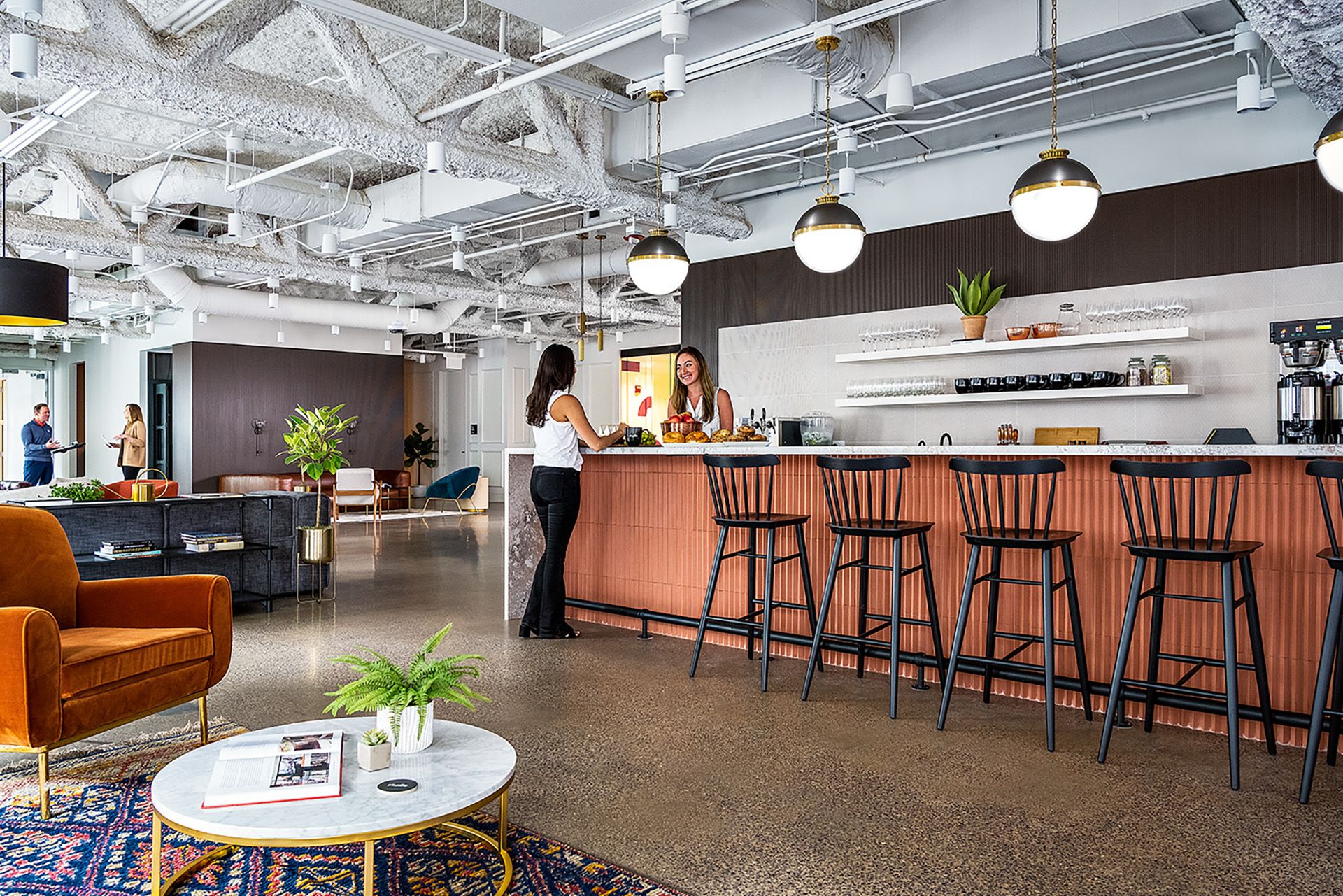 Modern office lounge area with bar counter, high chairs, and people talking