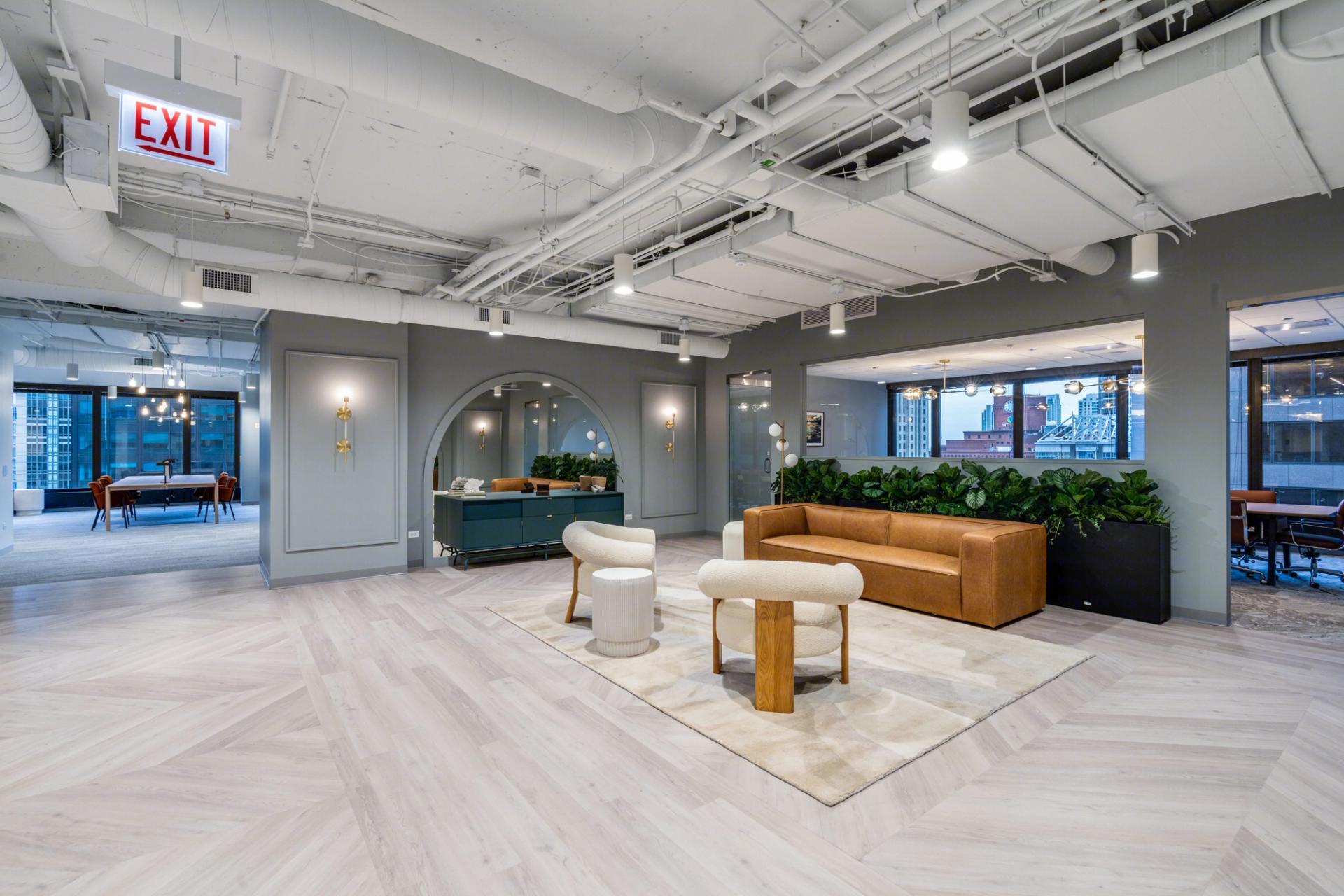 A modern office with a glass wall, wooden ceiling, and orange sofa, featuring a coffee table, plant, and desk, is illuminated by natural light and surrounded by a glass partition.