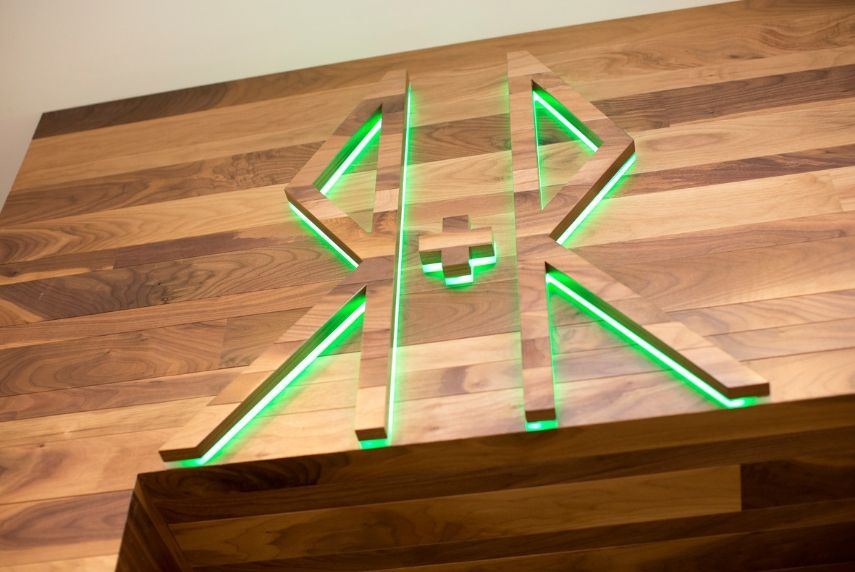 Wooden letters RR with a plus sign in the middle, backlit with green light on a wooden surface
