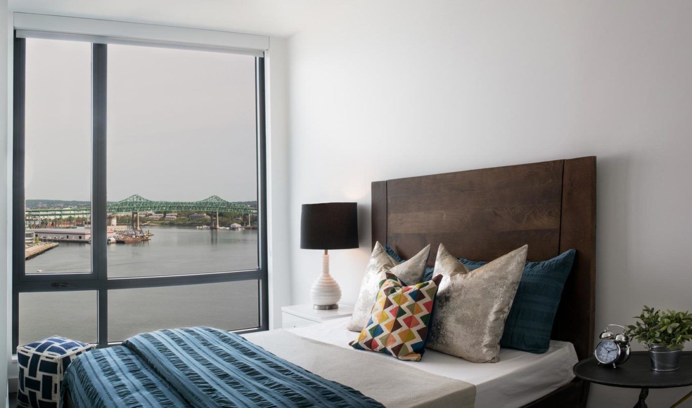 Model bedroom at The Eddy Apartments for rent in East Boston, featuring floor to ceiling windows with a view of the city.