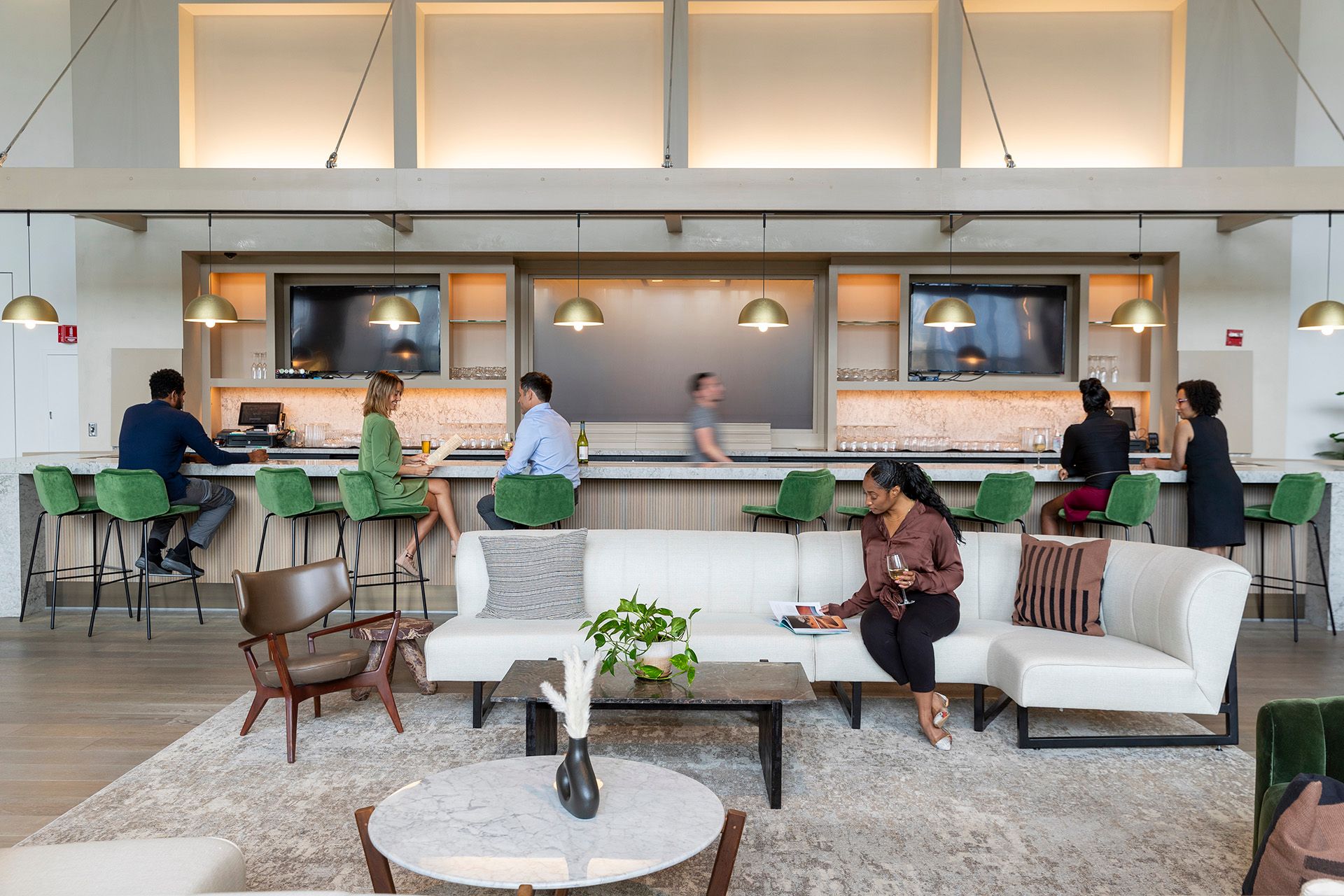 People sitting and chatting in a modern bar lounge with green bar stools and a curved white sofa