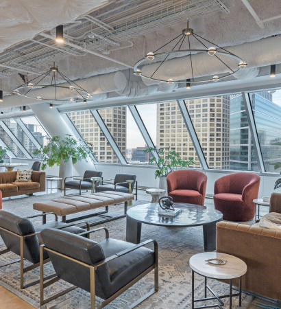 23rd floor clubhouse lounge at 525 West Monroe with floor-to-ceiling angled windows, leather and fabric seating in warm tones, round coffee tables, greenery, and modern circular chandeliers.
