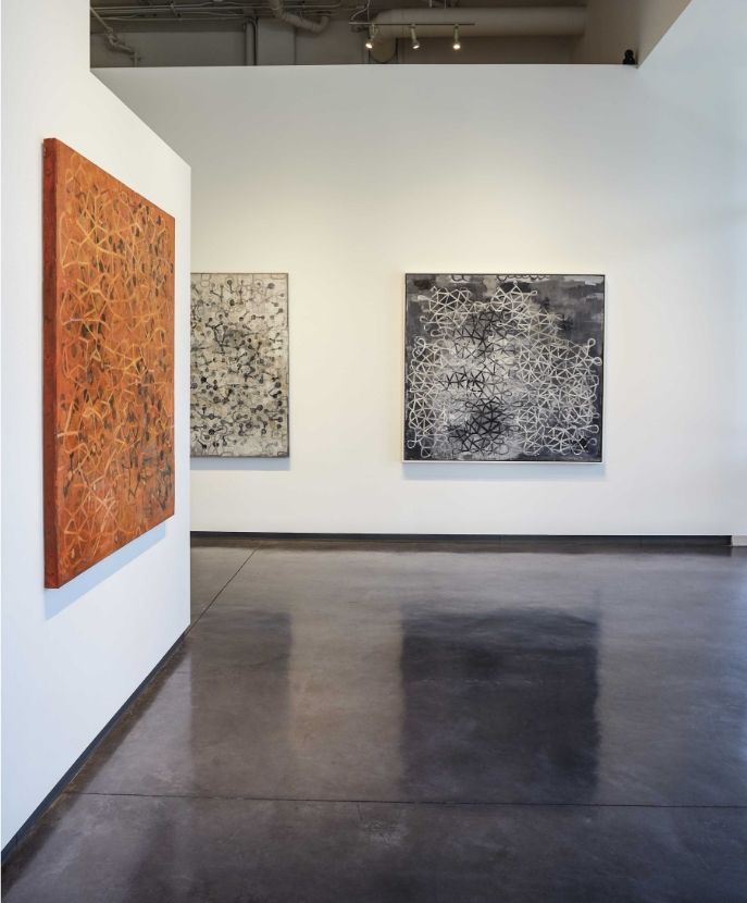 art gallery exhibition, with large-scale, textured abstract paintings displayed on white walls.