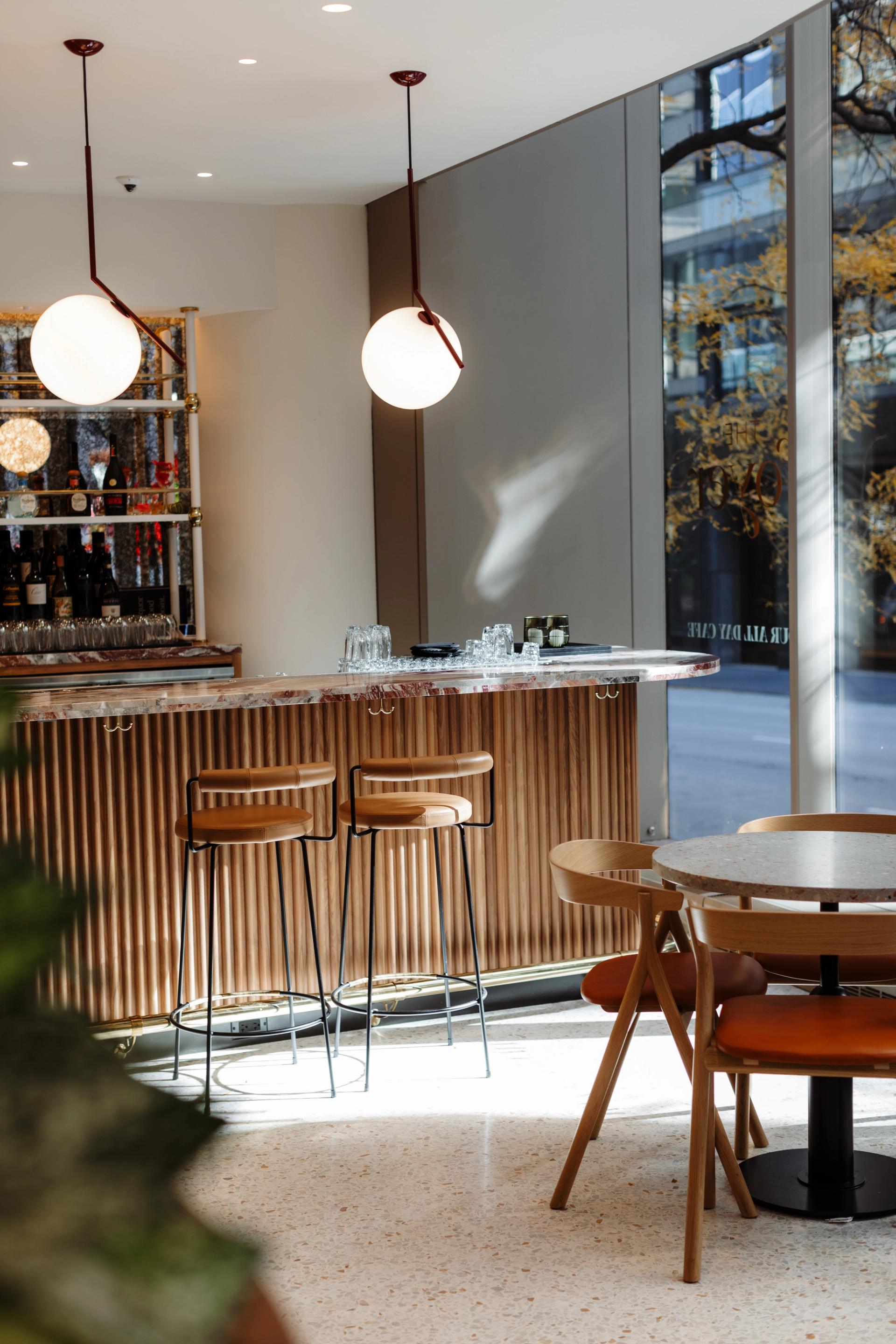 Bar and café area at 525 West Monroe with a wood-paneled counter, round globe pendant lights, bar stools, and tables with wooden chairs near tall windows.