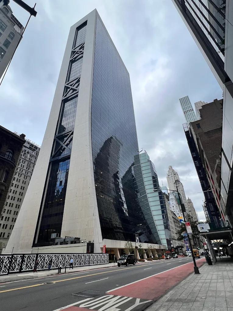 A bustling city street features a modern skyscraper with reflective glass, surrounded by other tall buildings and a traffic light, showcasing the city's dynamic energy and architectural diversity.