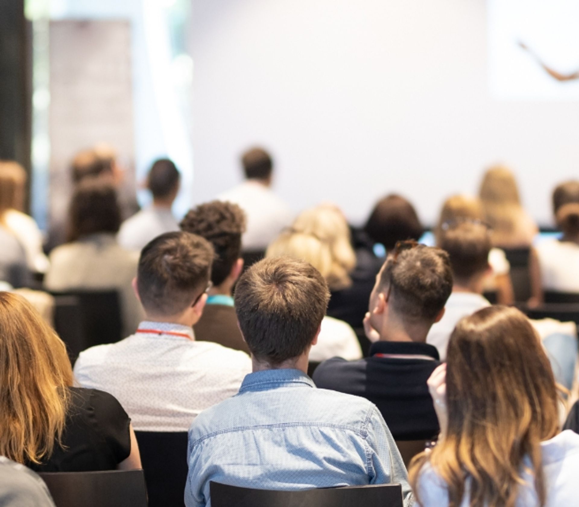 Audience of people seated and facing a presentation screen in a conference room