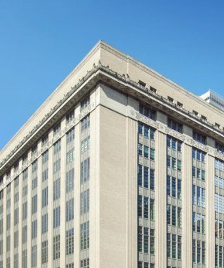 A large, multi-story brick building with tall windows and ornate detailing under a clear blue sky.