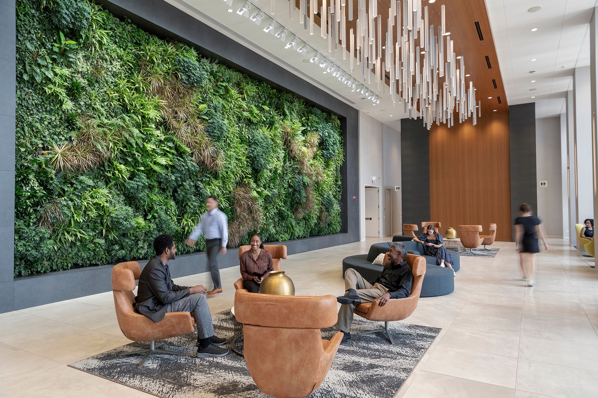 People sitting and talking in a modern lobby with a large green plant wall and unique hanging ceiling lights