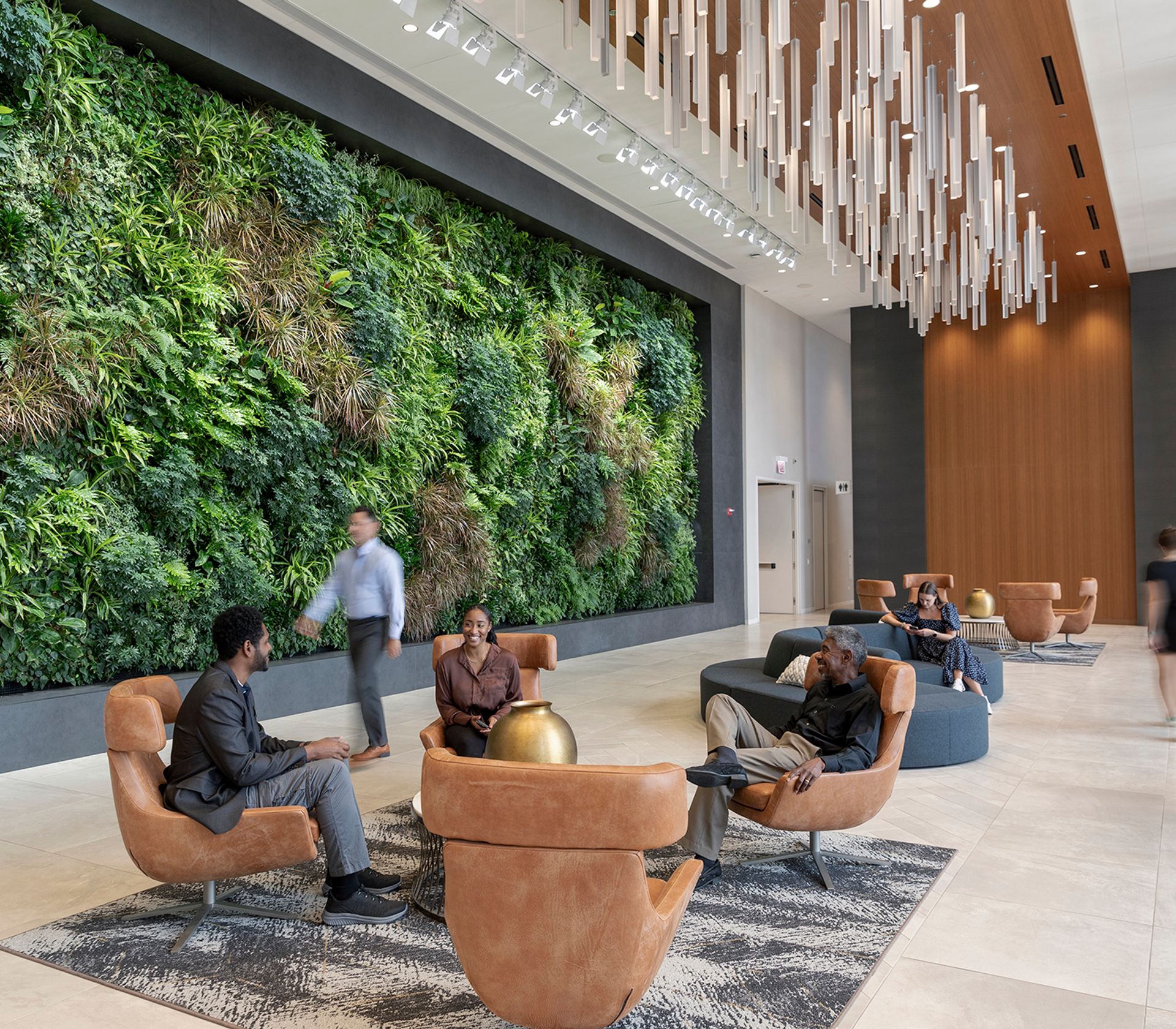 People sitting and talking in a modern lobby with a large green plant wall and unique hanging ceiling lights