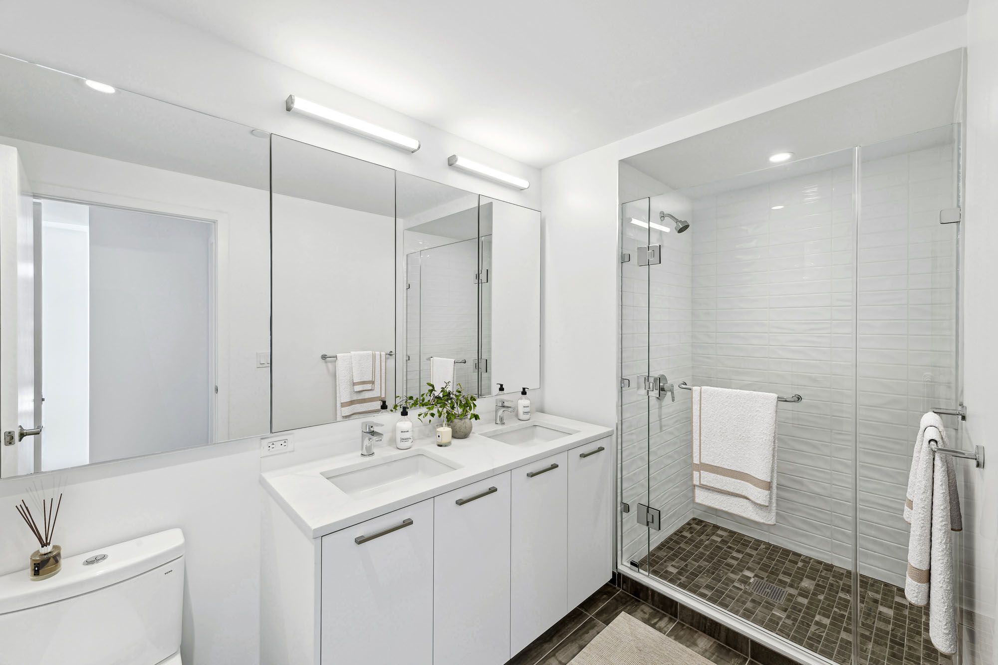 Model bathroom at Crossing DC apartments in Navy Yard, featuring white counters and tiled shower with a glass door.