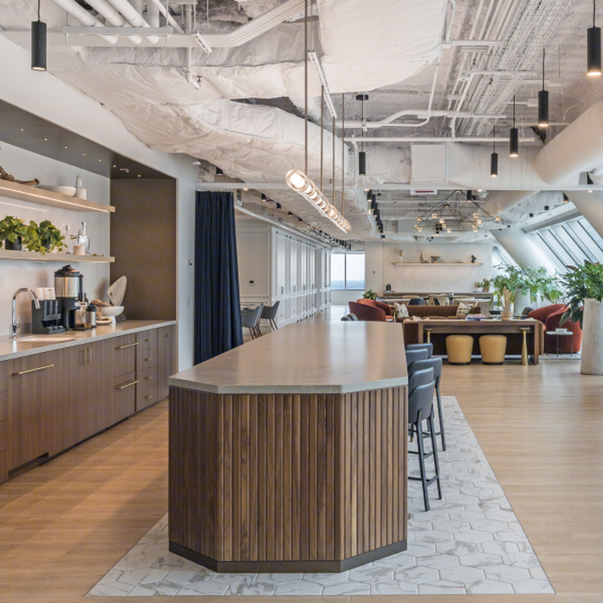 23rd floor clubhouse at 525 West Monroe with a long wooden island counter, built‑in coffee station, modern lounge seating, greenery, and exposed industrial ceiling design.