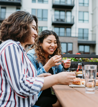 People sitting at an outdoor patio table near 525 West Monroe, enjoying food and drinks with modern residential buildings in the background.