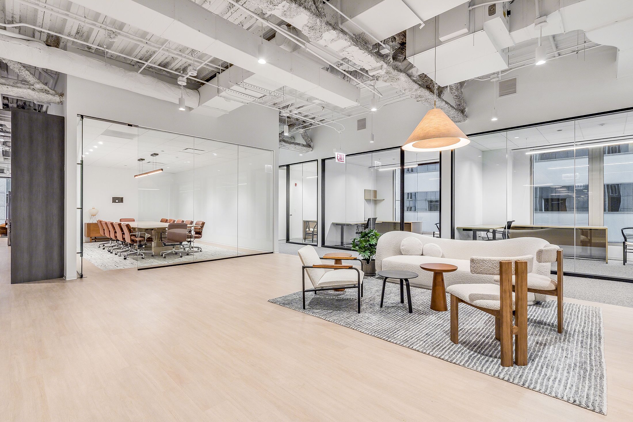 Modern office lounge area with white chairs, a sofa, tables, and a glass-walled conference room in the background