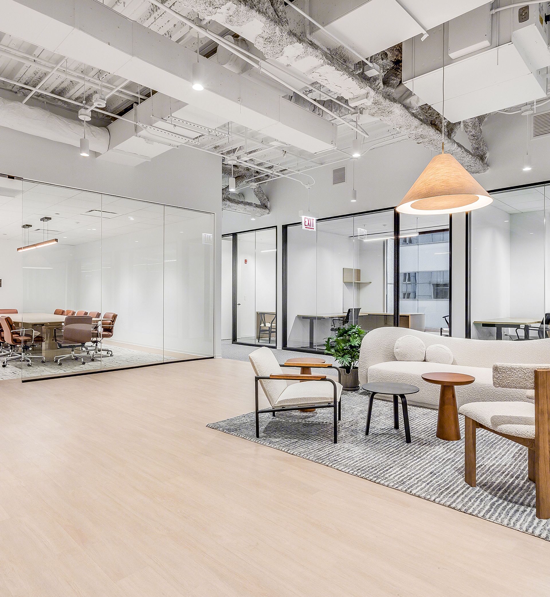 Modern office lounge area with white chairs, a sofa, tables, and a glass-walled conference room in the background