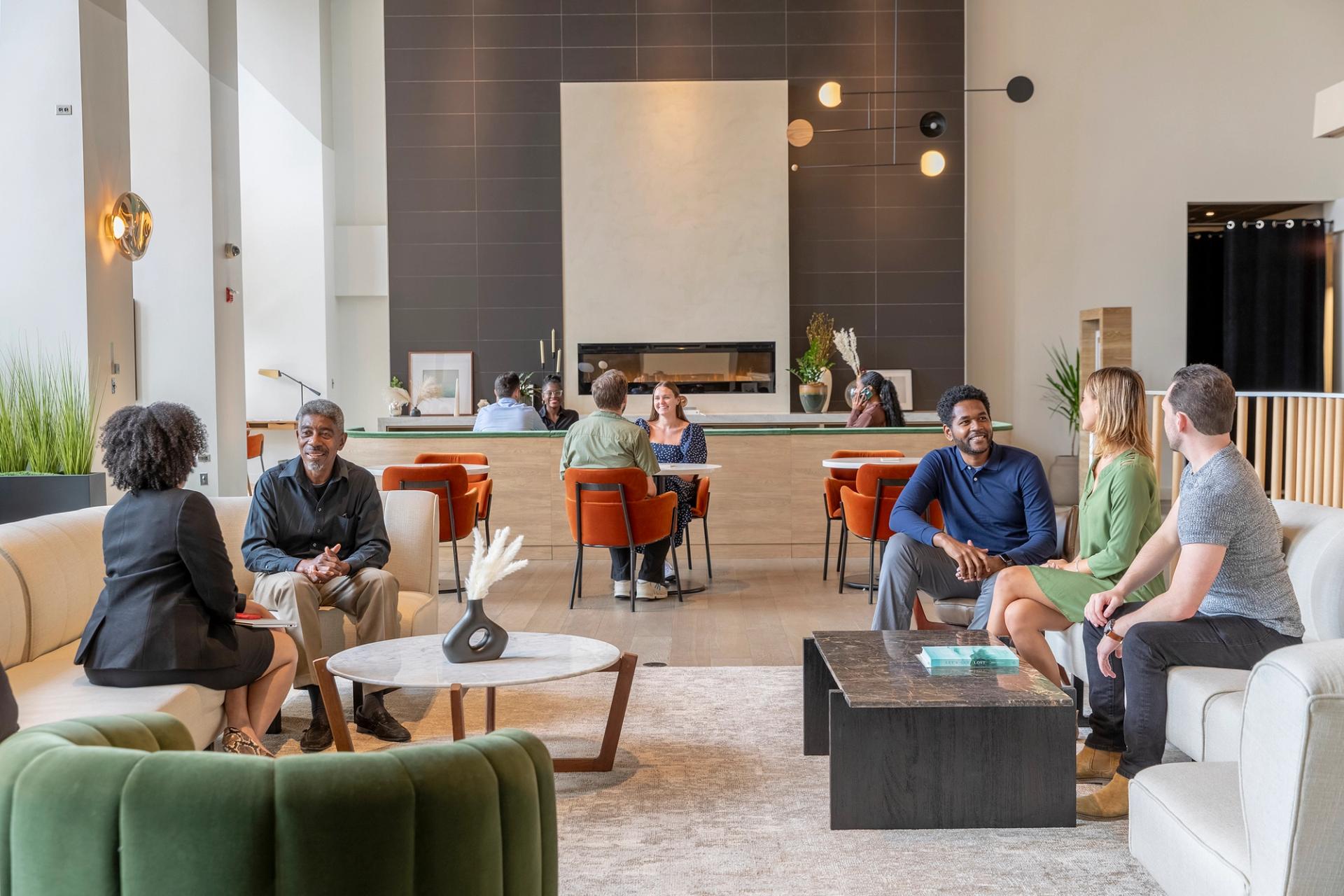 People sitting and talking in a modern, cozy lounge area with a fireplace and orange chairs