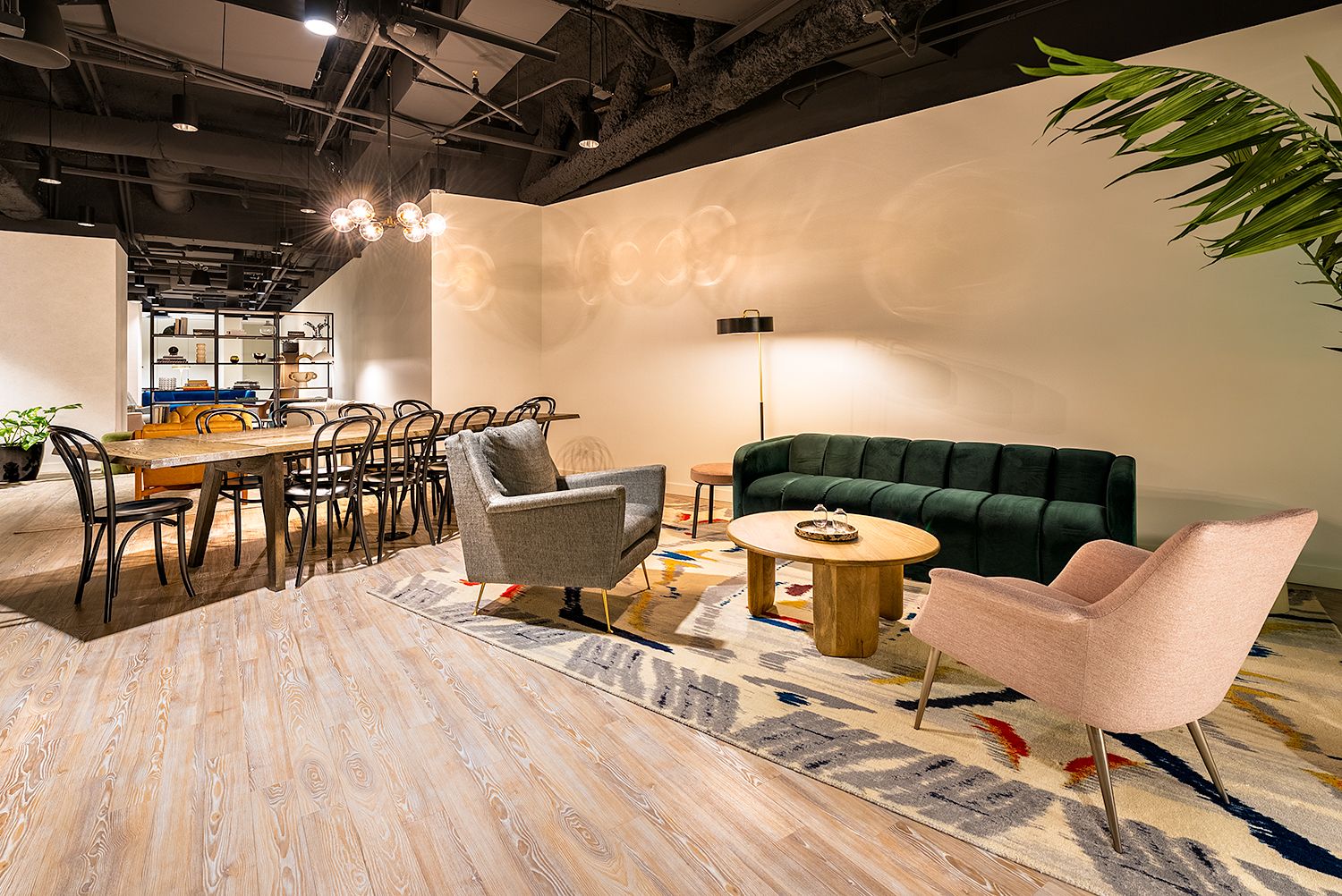 Modern living room with green sofa, gray and pink chairs, wooden coffee table, and dining area with wooden table and black chairs