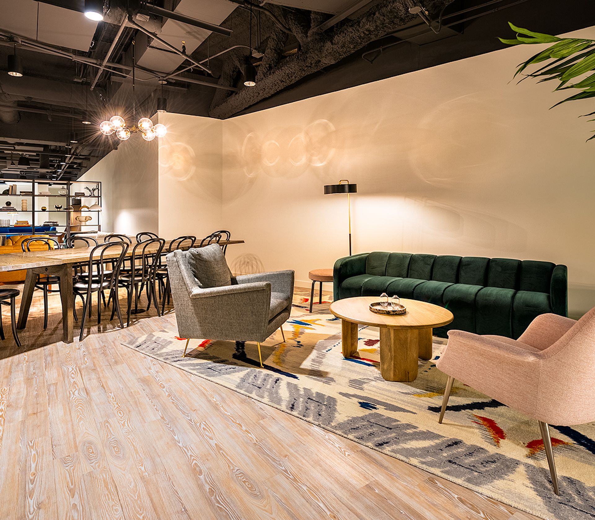 Modern living room with green sofa, gray and pink chairs, wooden coffee table, and dining area with wooden table and black chairs