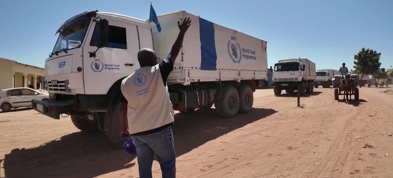 Humanitarian worker stands on a road in Sudan next to a large World Food Programme lorry